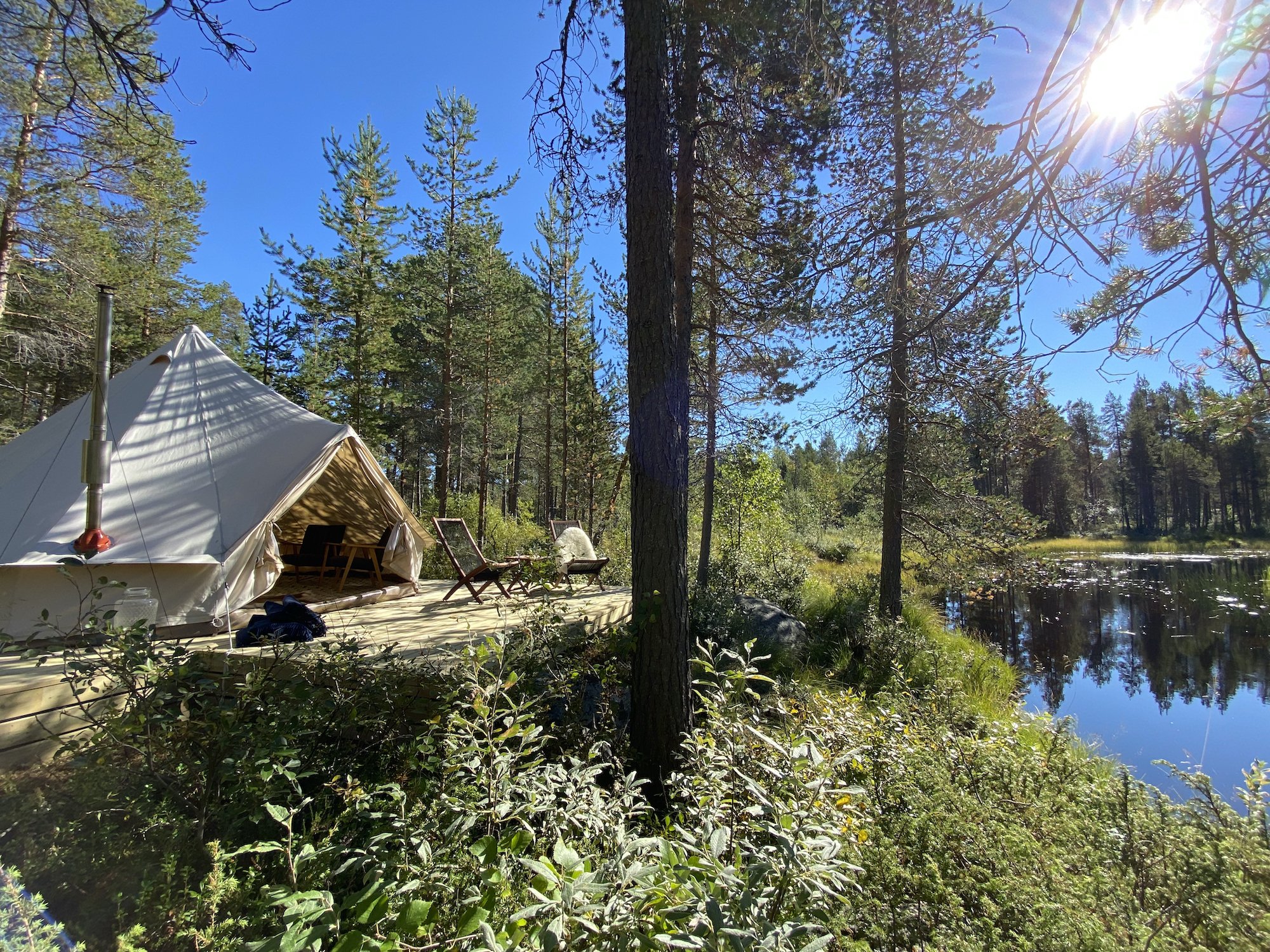 Telt med tredekk i skogen nær en innsjø, solrik dag