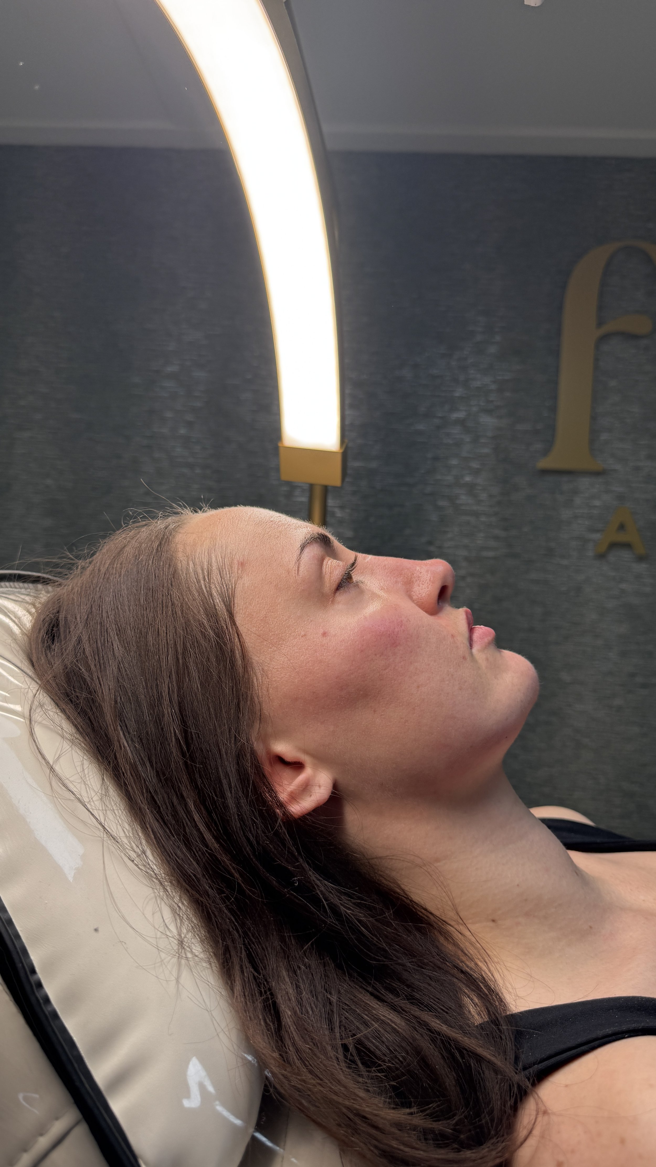 Woman lying on a medical or spa treatment bed with a large light above her face.