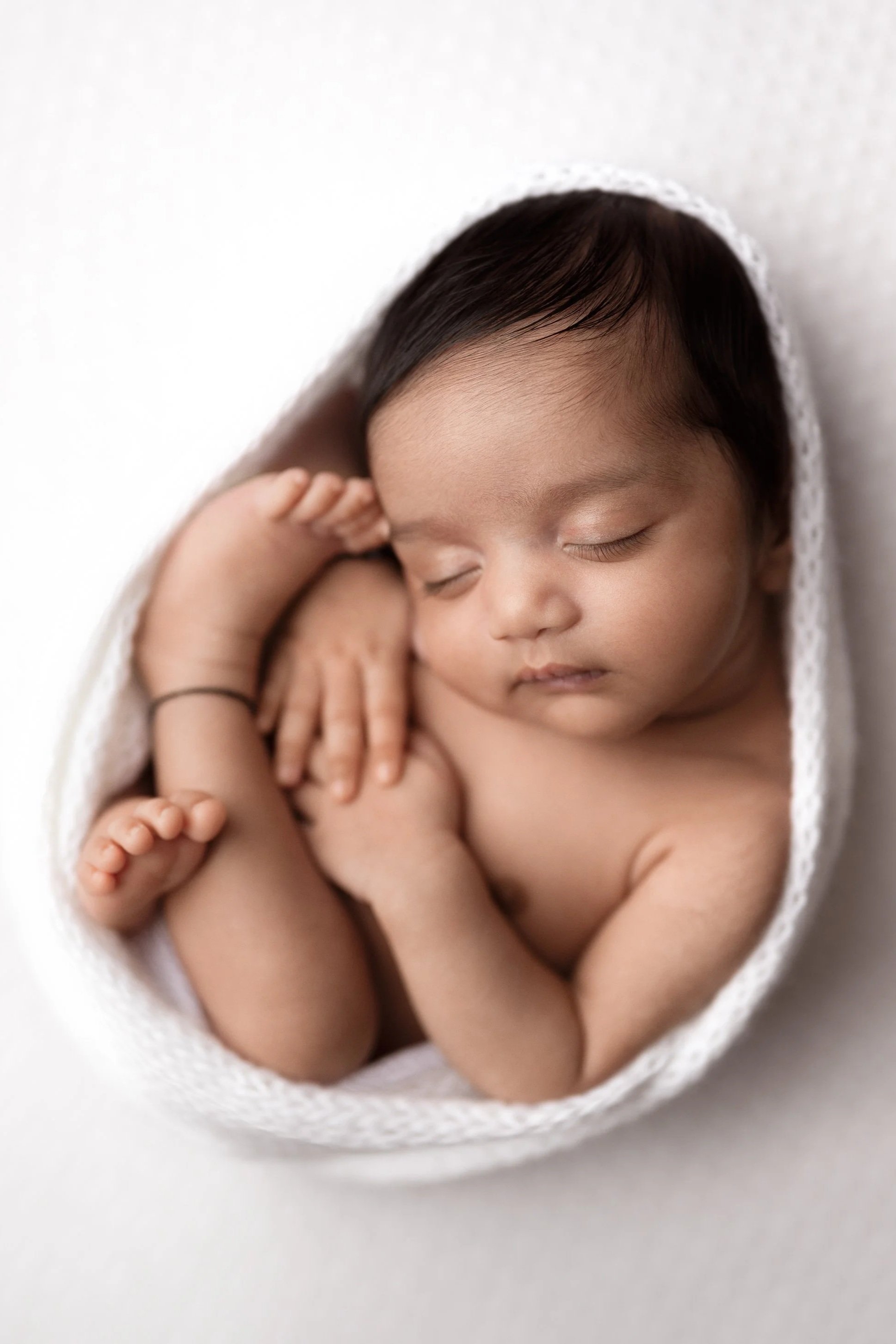 A sleeping baby with dark hair swaddled in a white blanket.