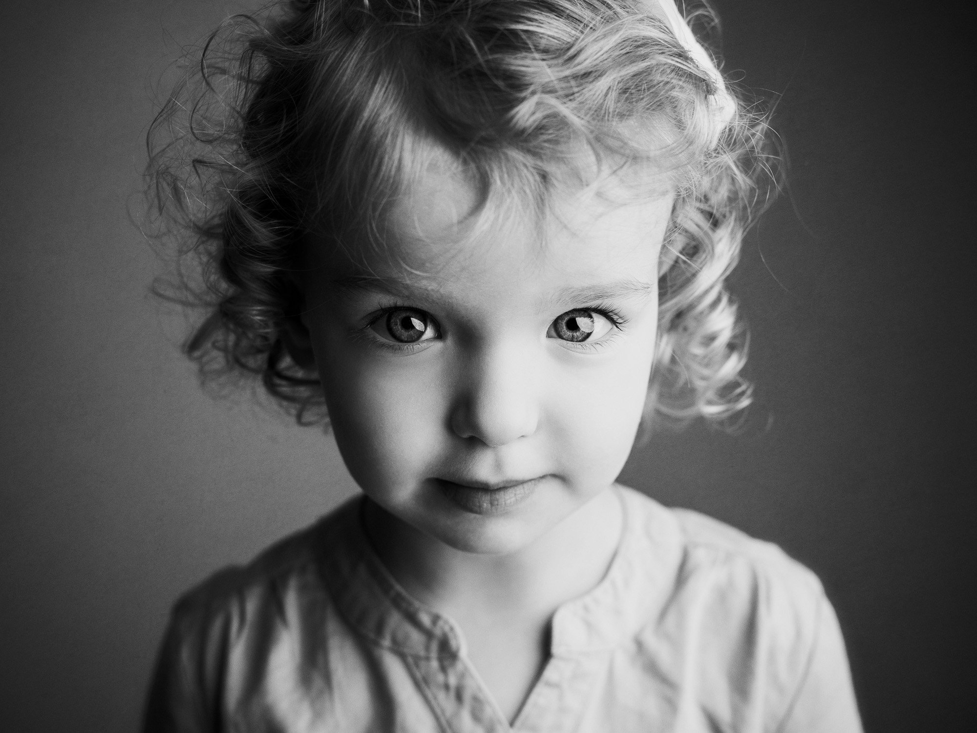 Black and white photo of a young girl with curly hair and light eyes, looking directly at the camera.
