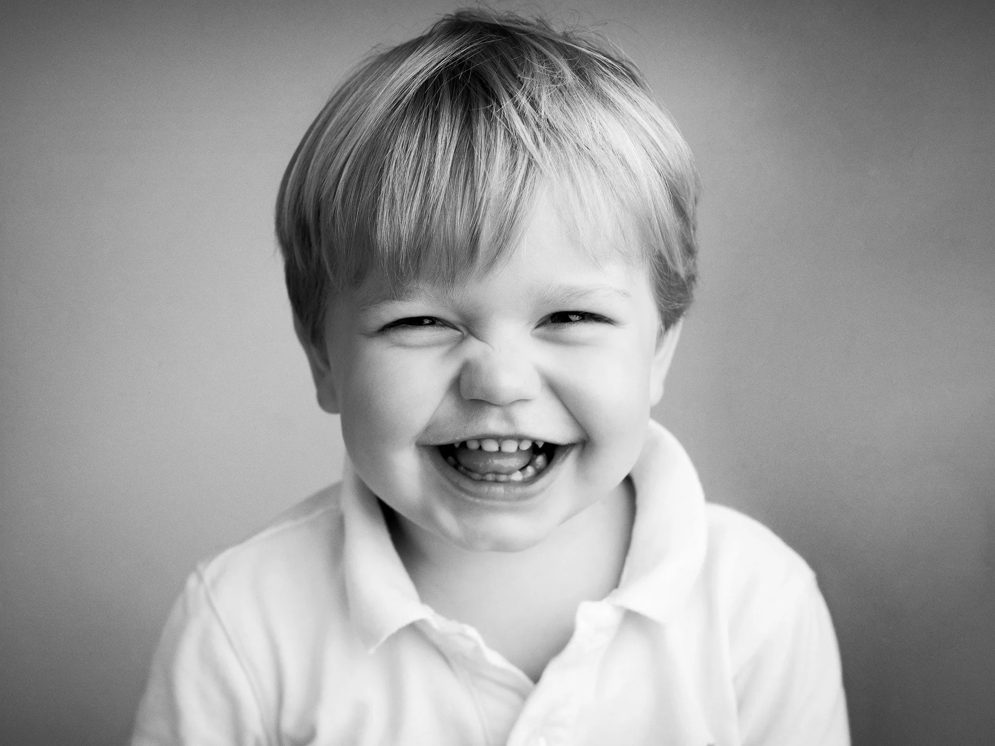 Black and white photo of a smiling young boy with short hair, wearing a collared shirt.