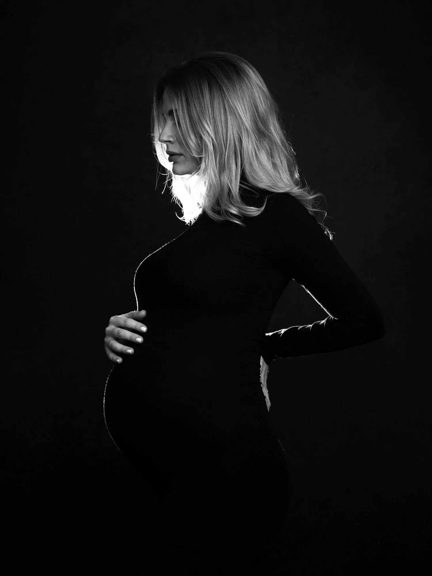 Silhouette of a pregnant woman with her hand on her belly, in black and white.