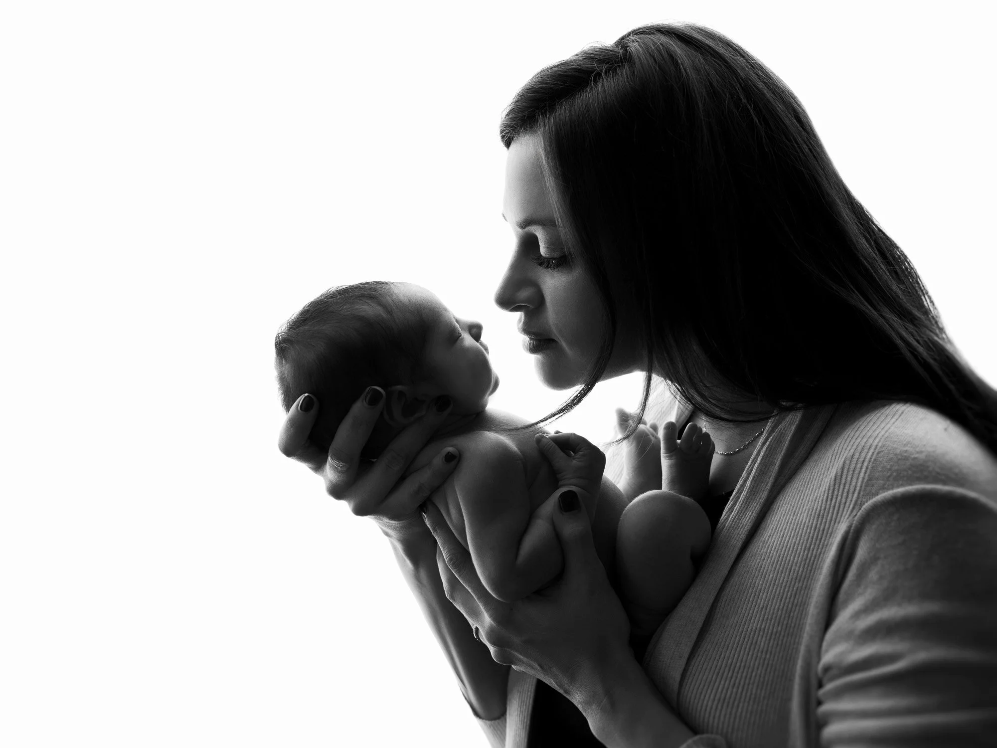 A woman holding a newborn baby close to her face, looking into the baby's eyes in black and white.
