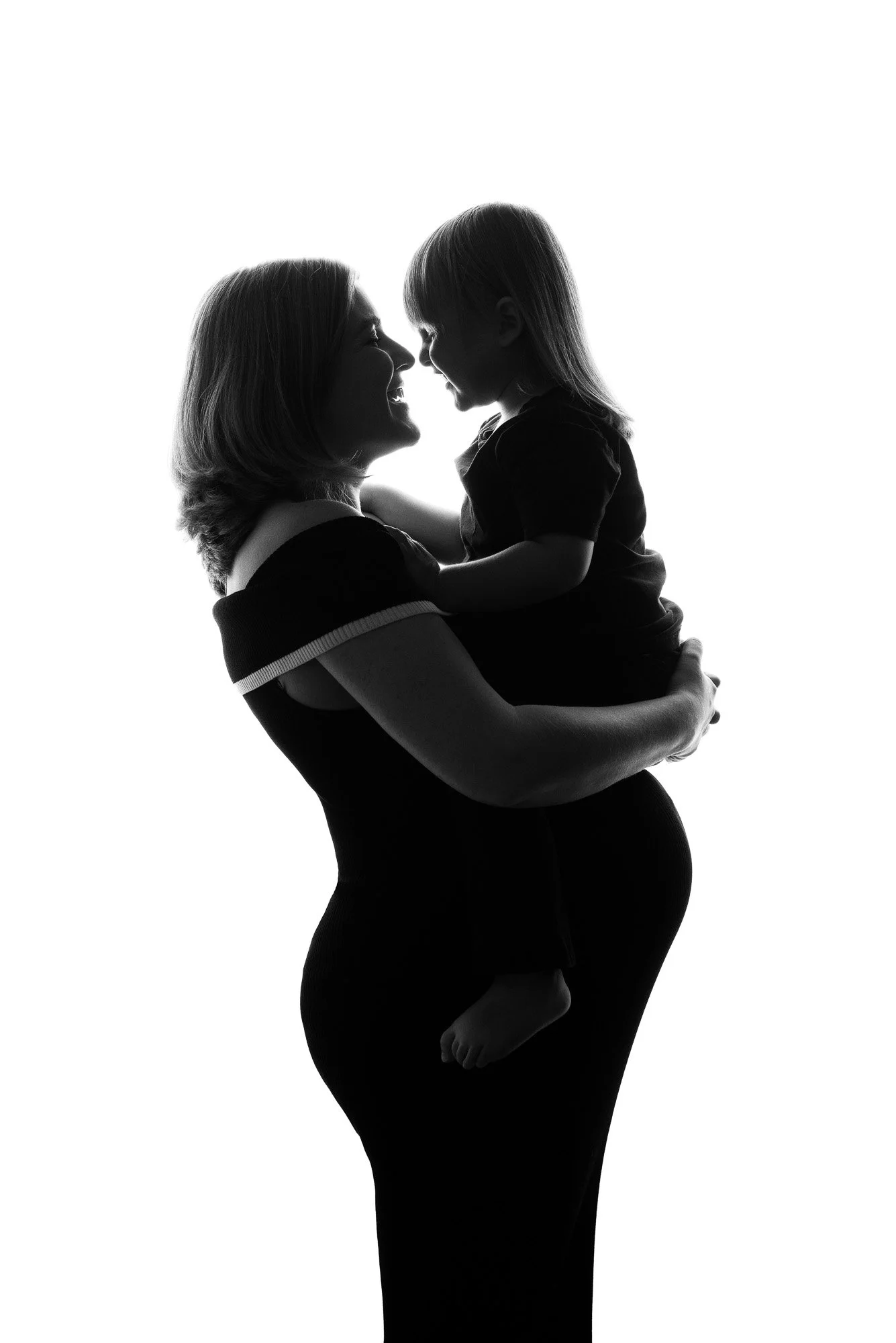 A woman holding a child in her arms, both smiling and touching nose to nose, in a black and white silhouette against a white background.
