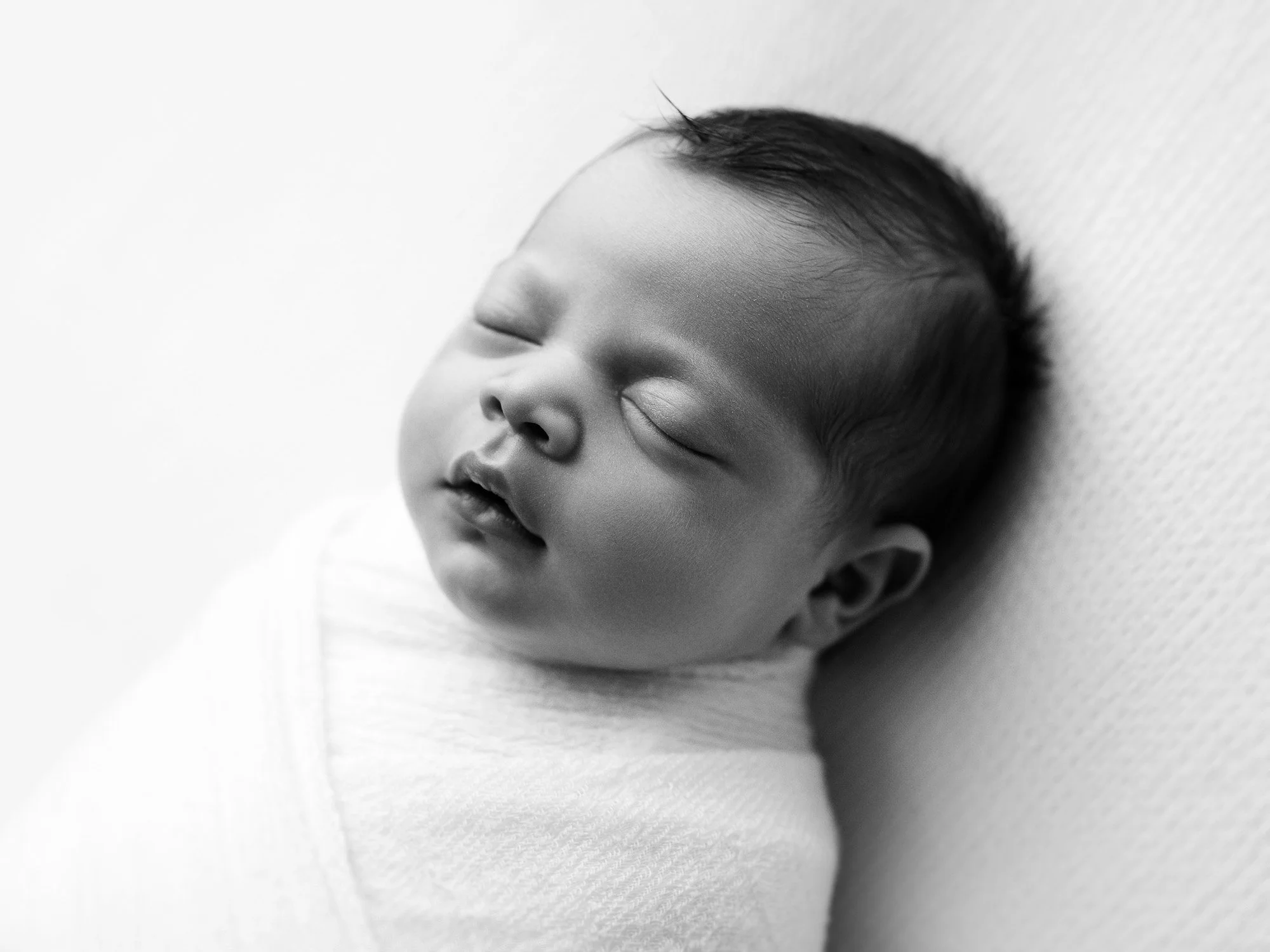 Close-up of a sleeping newborn baby wrapped in a blanket, lying against a textured surface.