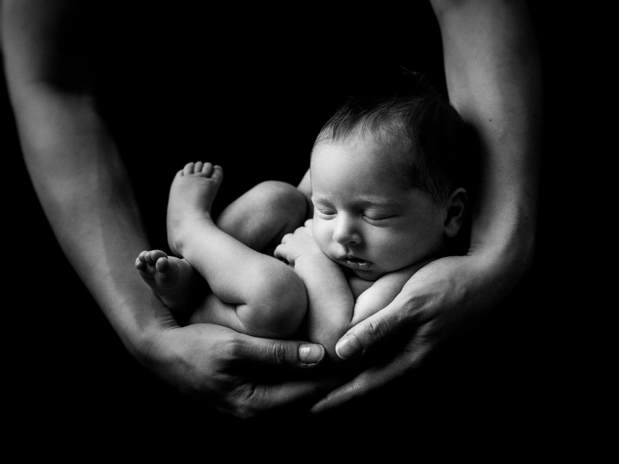 Black and white photo of a newborn cradled in adult's hands, sleeping peacefully.
