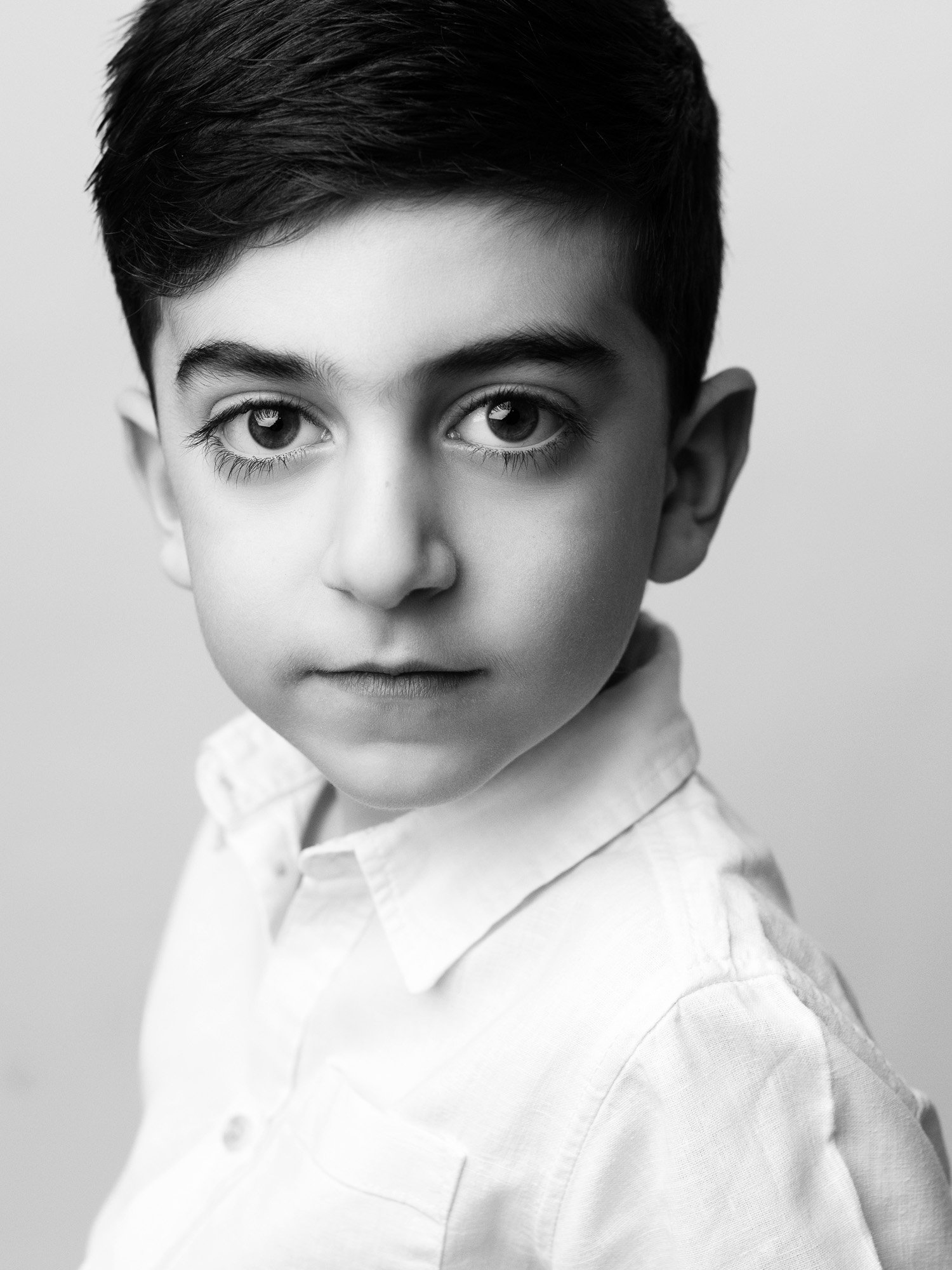 Black and white portrait of a young boy with short dark hair, wearing a collared shirt, looking directly at the camera with a serious expression.