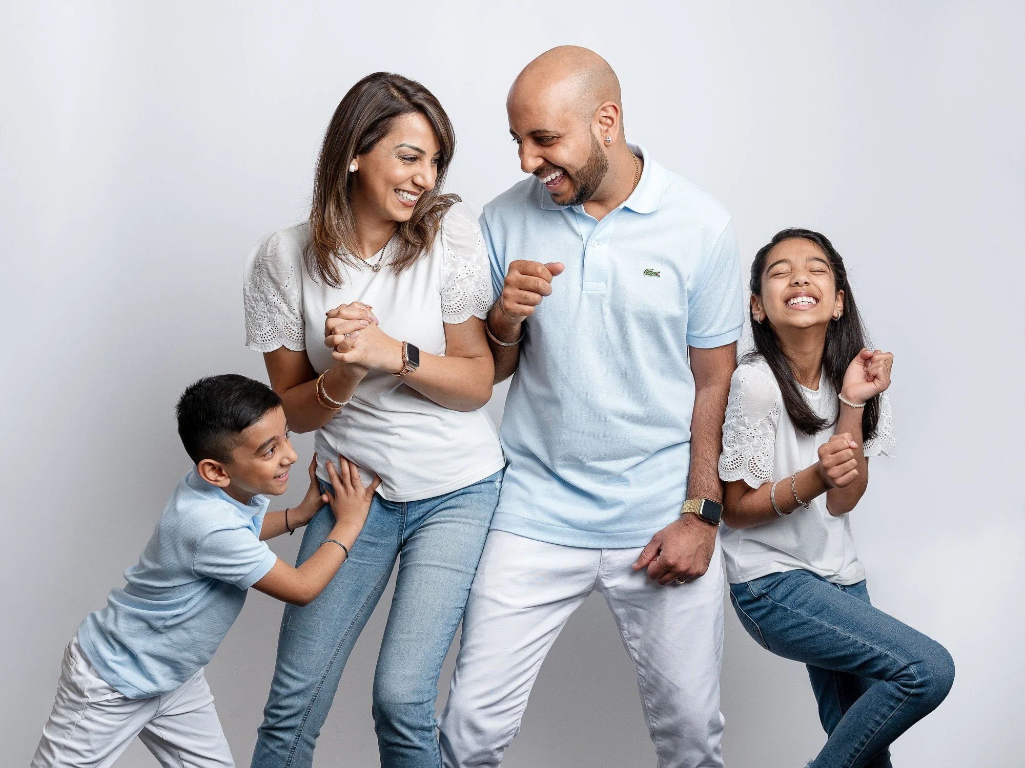 A happy family of five, including two children, a woman, a man, all smiling and playfully interacting against a white background.