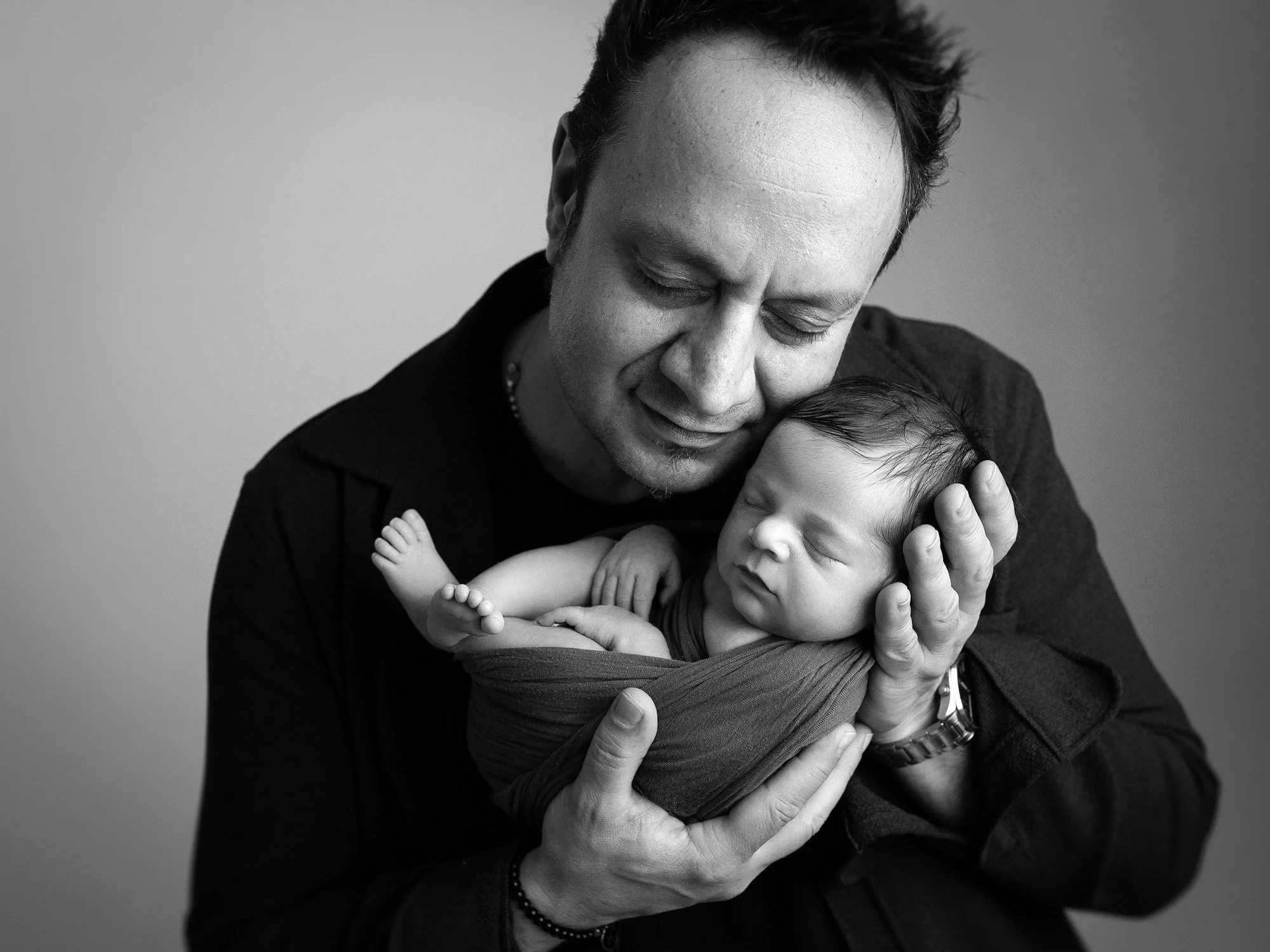 A man holding a sleeping baby close to his face, with both appearing peaceful in a black and white photo.