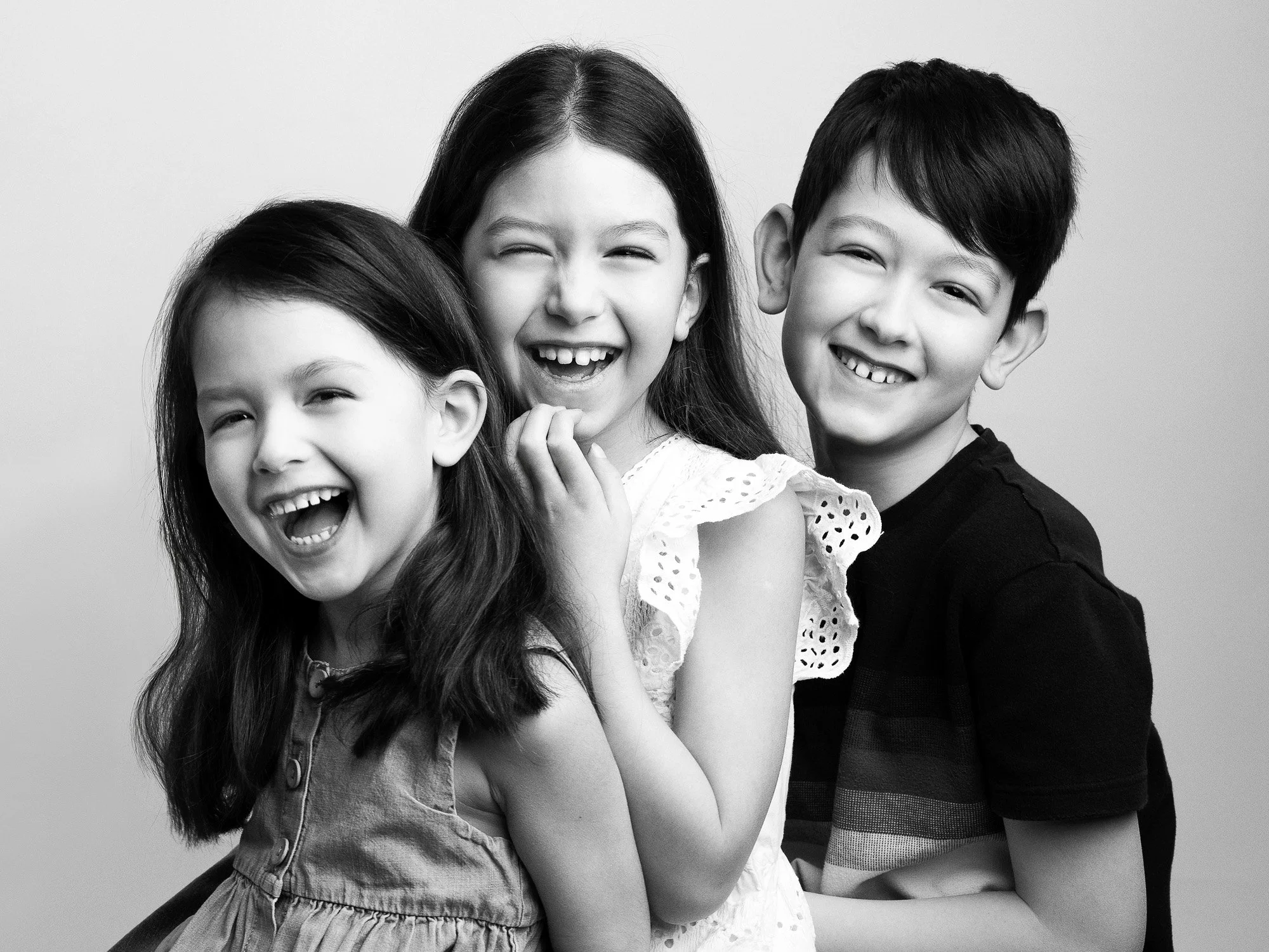 Three children laughing and posing together in a black and white photo.