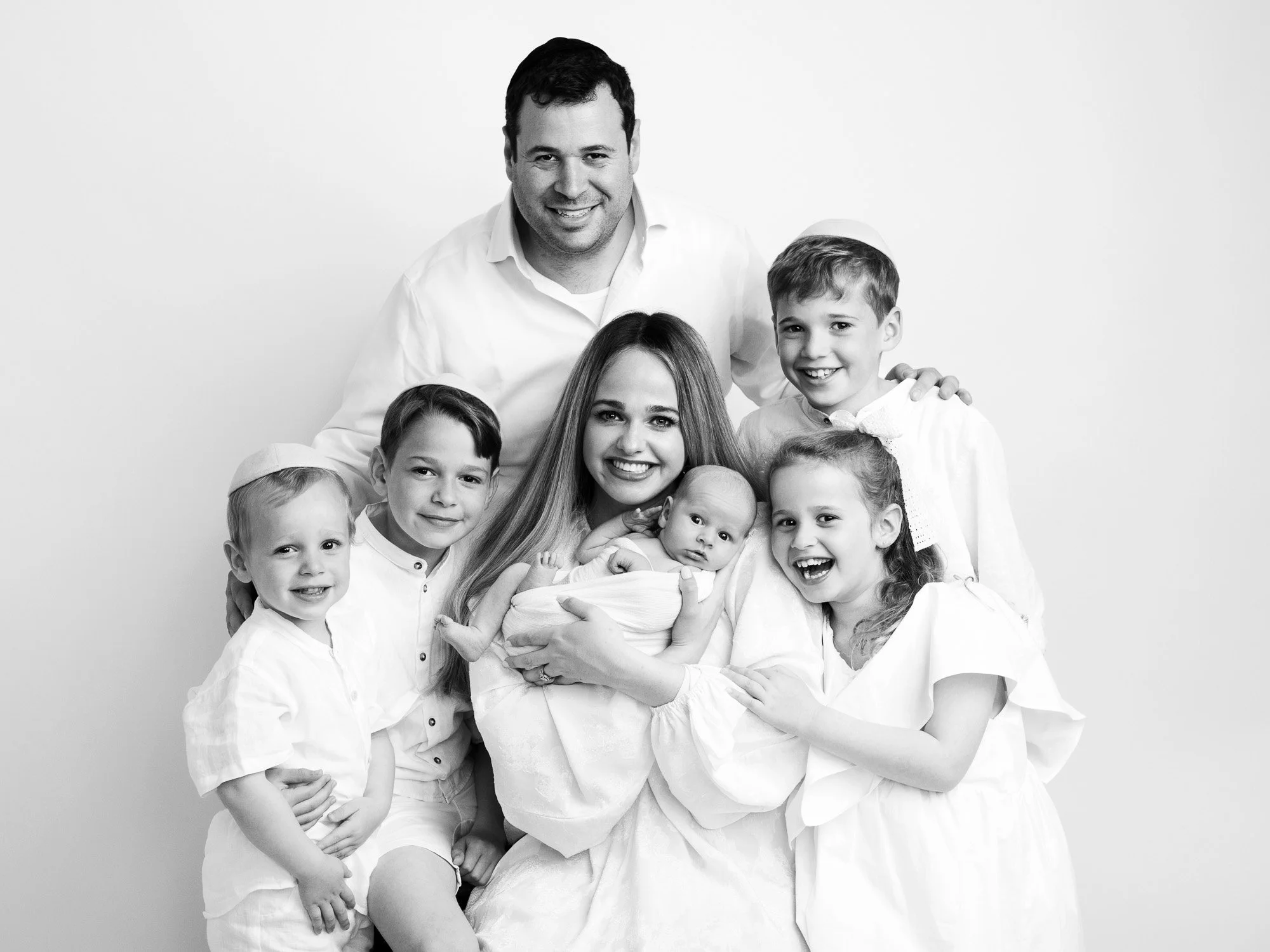 Family of eight, including parents, four children, and two babies, smiling together in a portrait