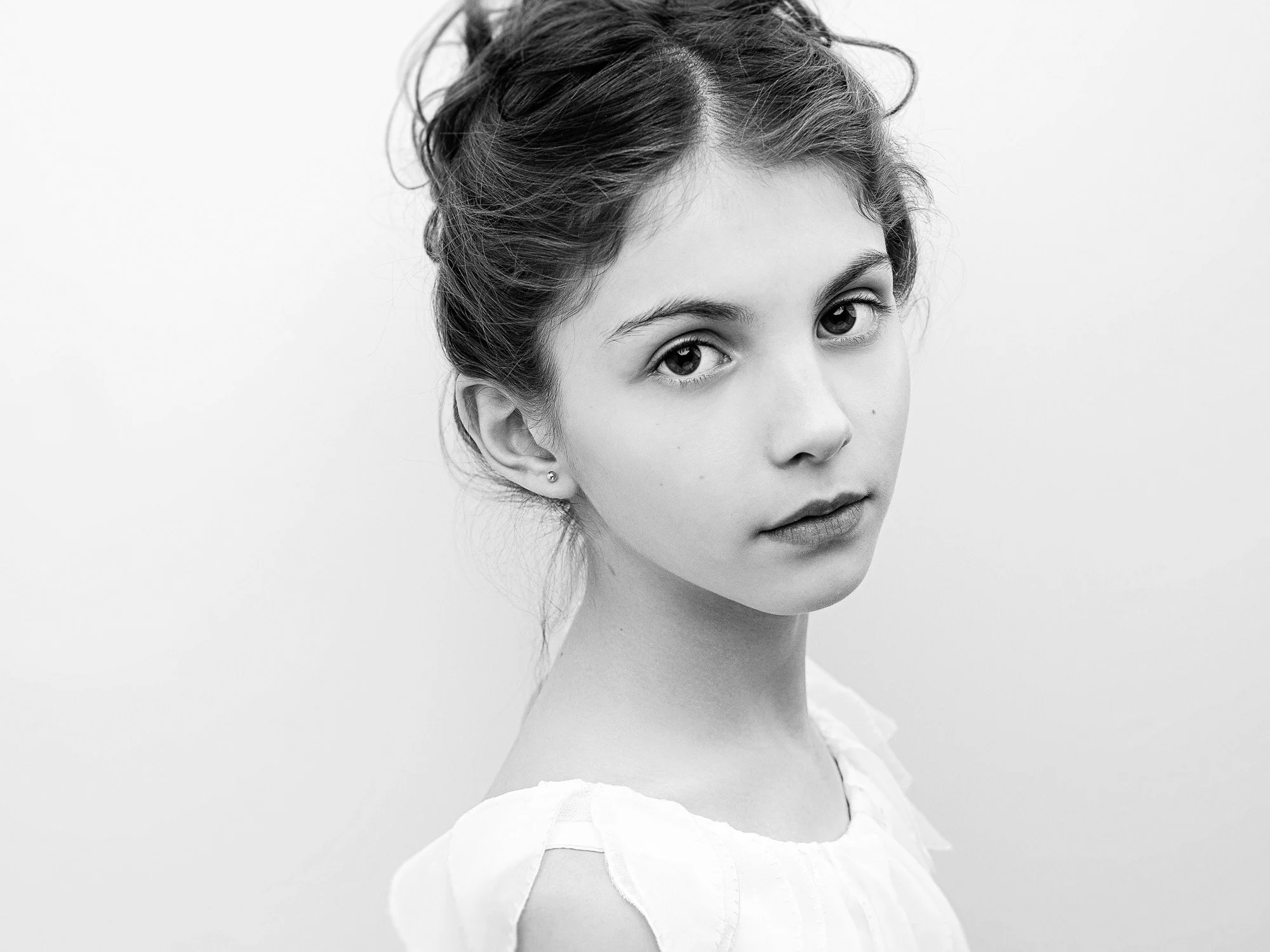 Black and white portrait of a young woman with her hair up, looking directly at the camera, wearing a light-colored top.