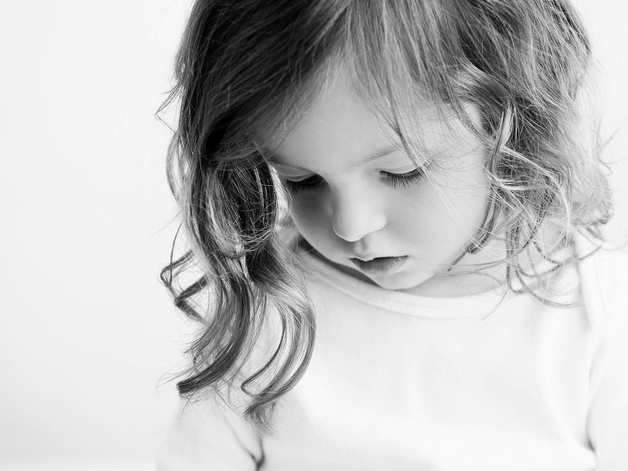 Close-up of a young girl with curly hair looking downward in black and white.