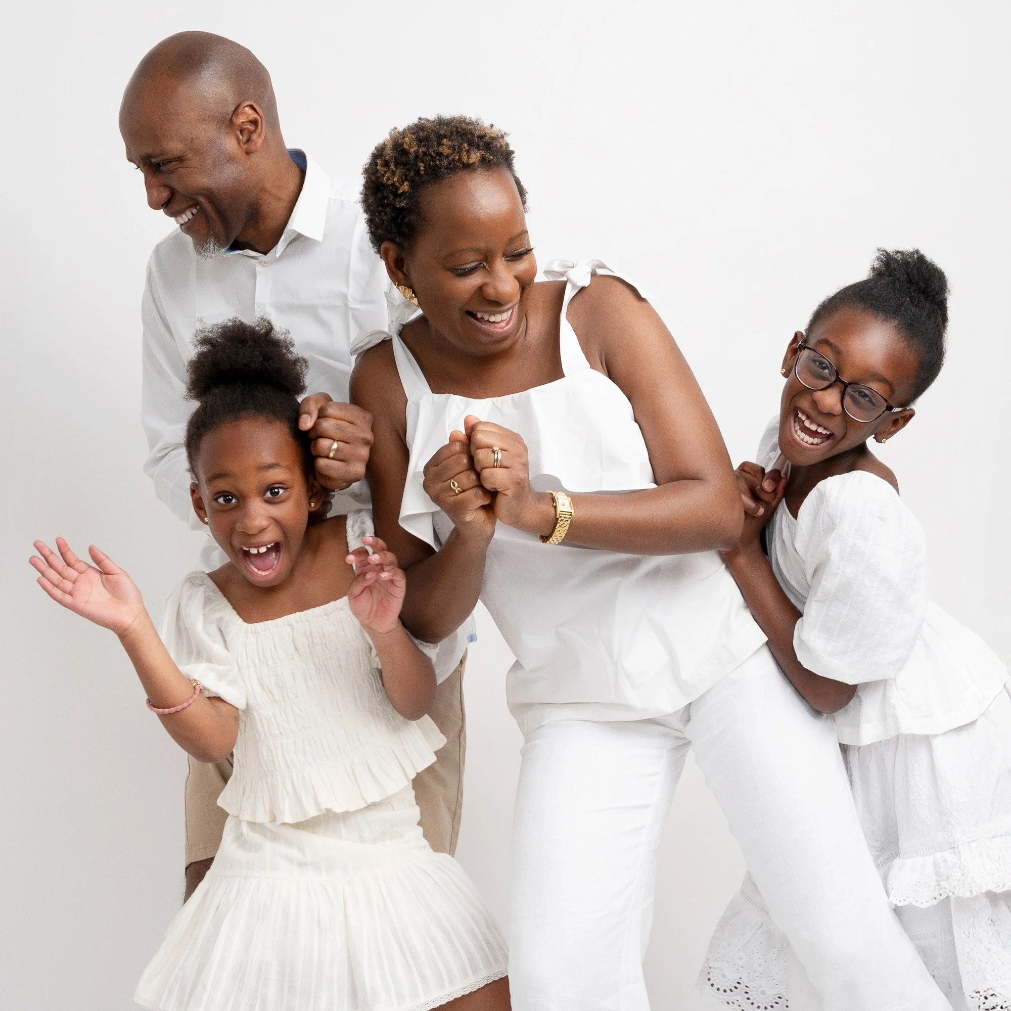 A happy multigenerational African American family of four having fun and smiling against a white background, dressed in white clothes.