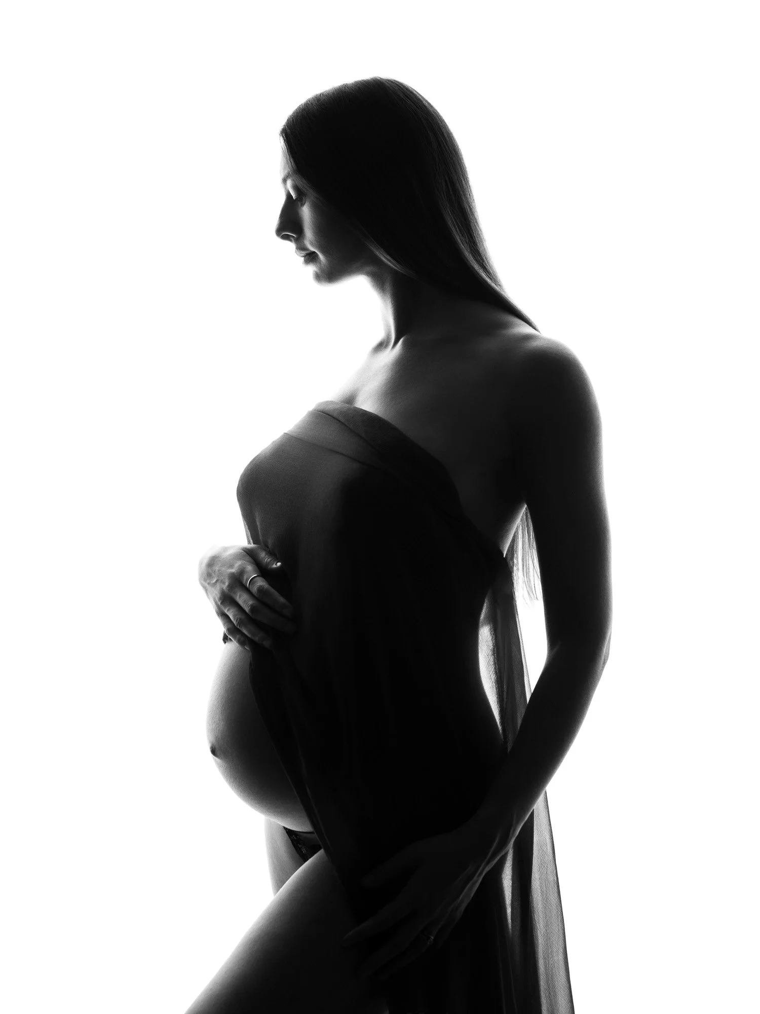 Silhouette of a pregnant woman in profile, draped in sheer fabric, standing against a white background.