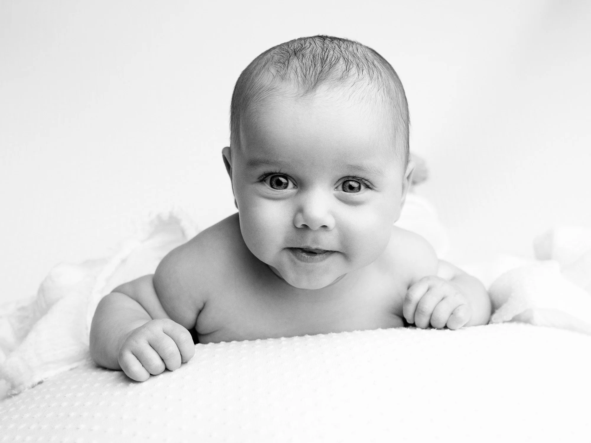 A baby lying on a soft surface, looking at the camera, with a curious expression.