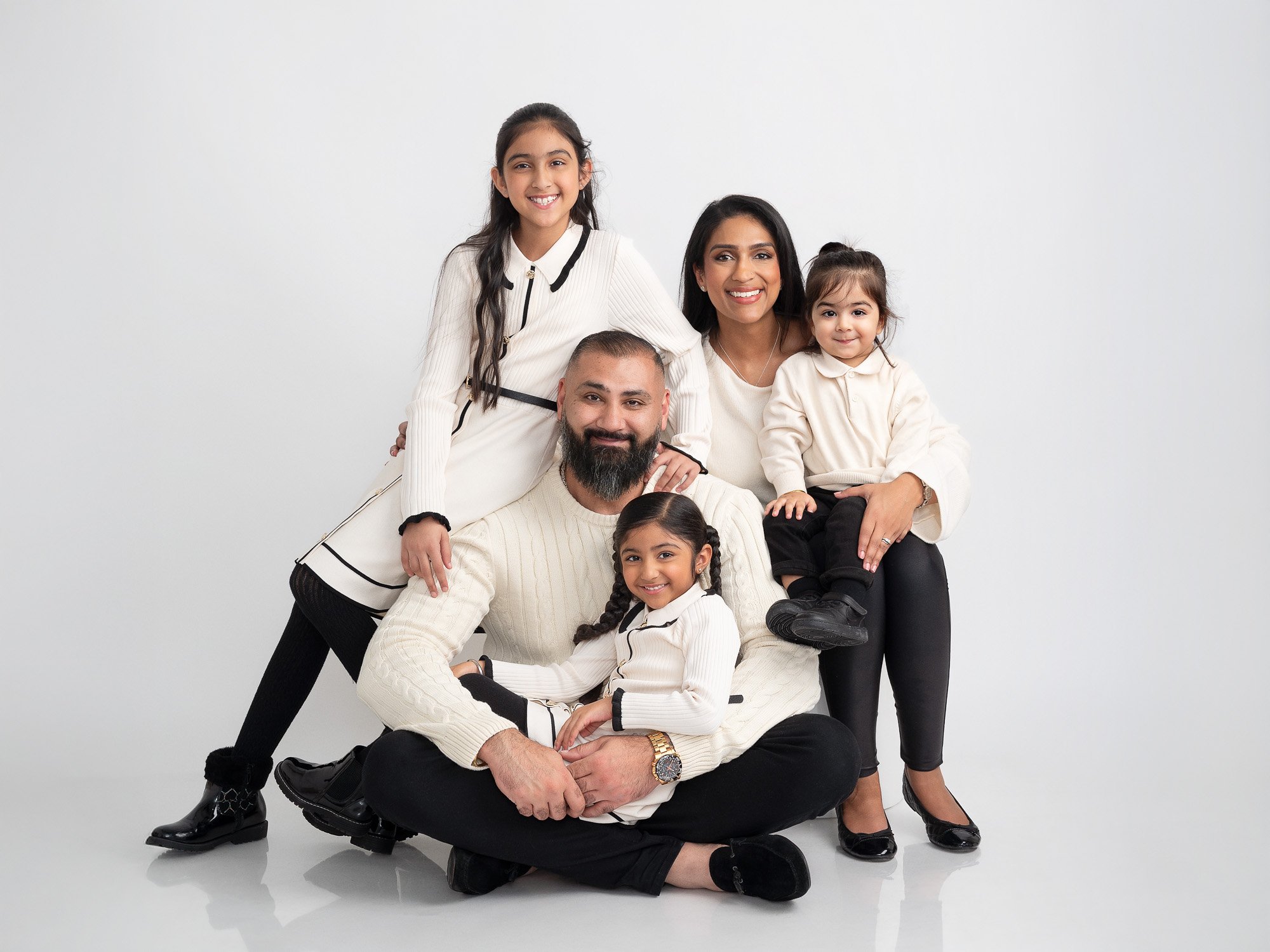A diverse family of six posing together against a white background, smiling and dressed in coordinated white and black outfits.