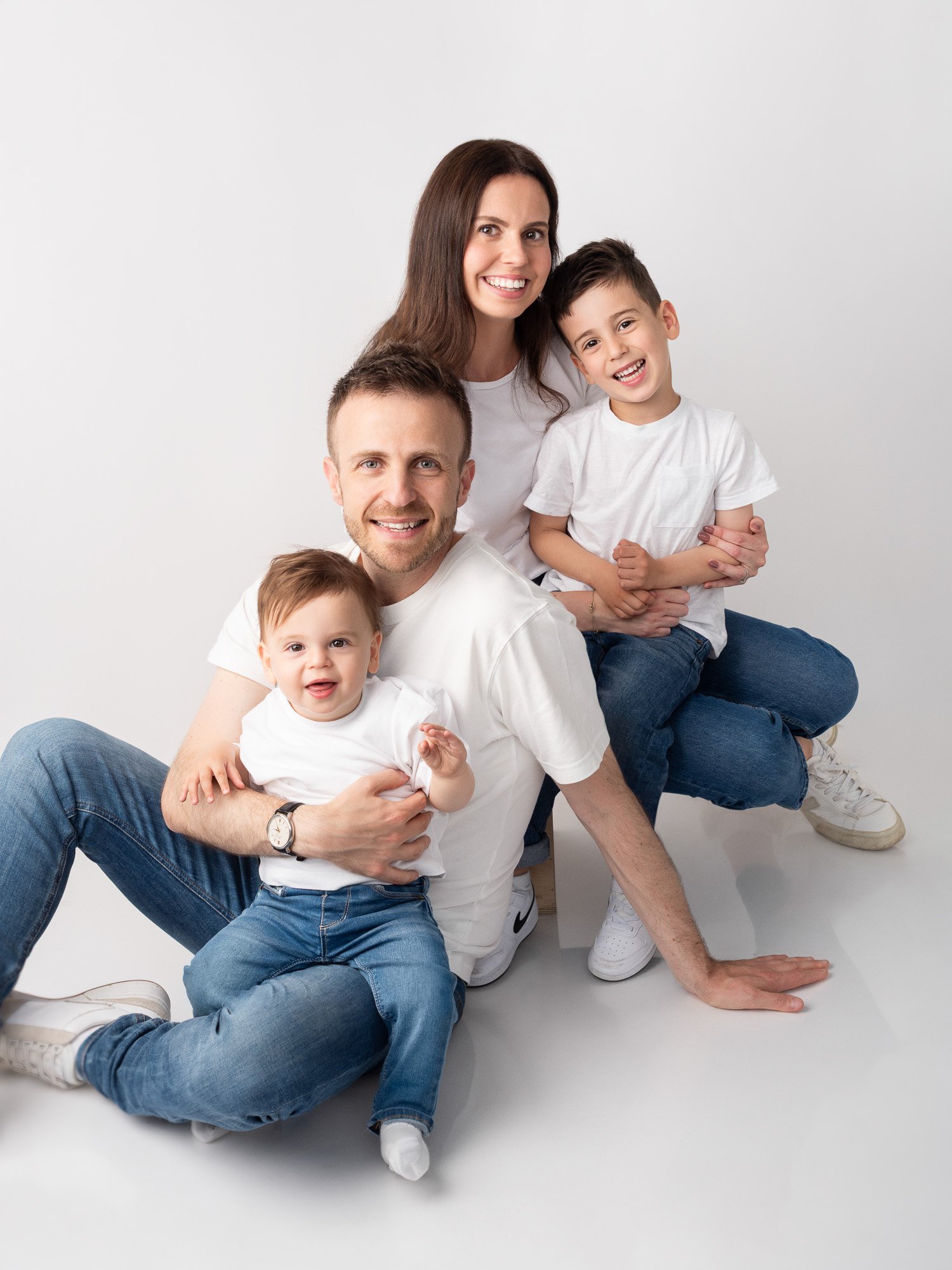 A happy family of four posing together in a photo studio with a white background, including a woman, two boys, and a man.