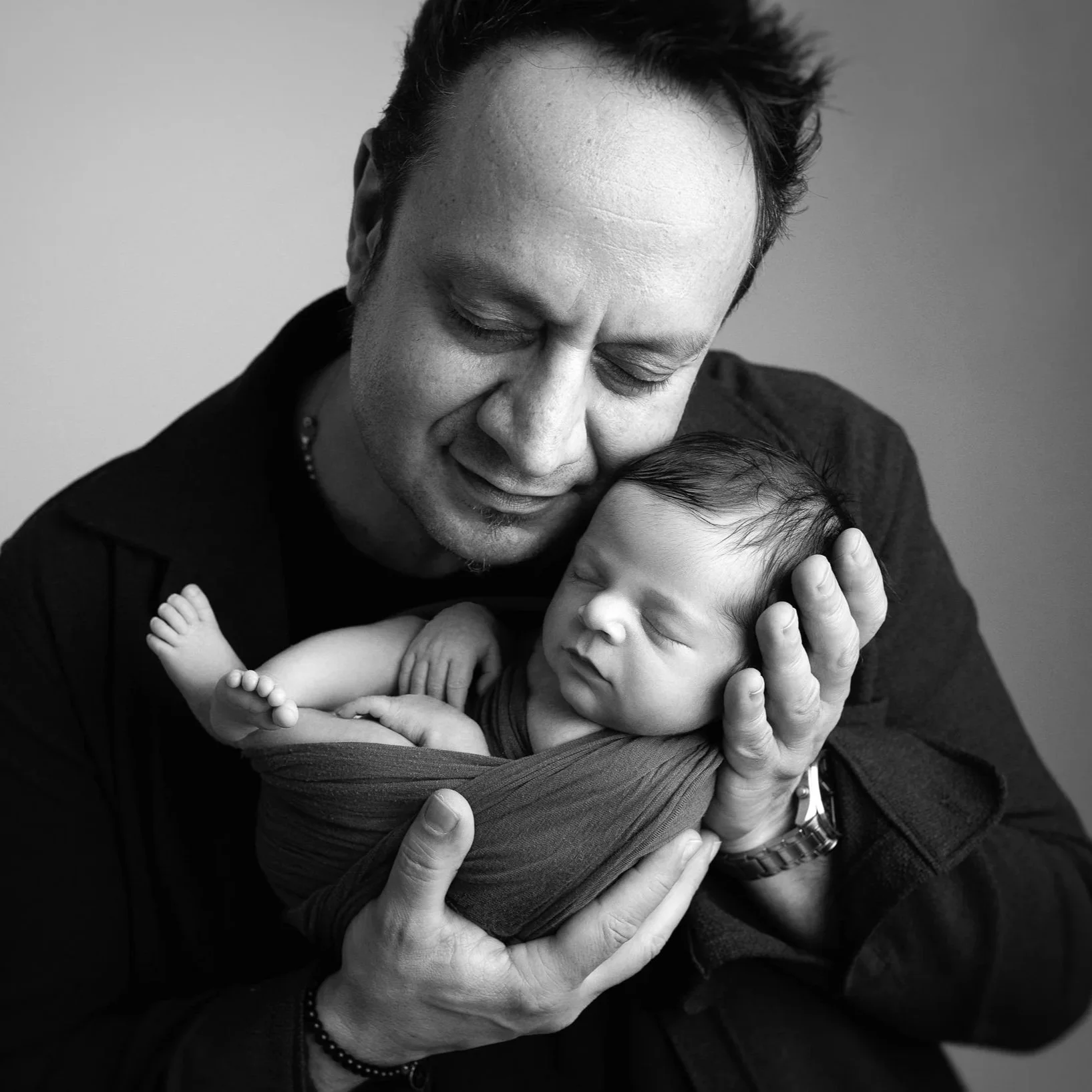 A black and white photo of a man gently holding a sleeping baby in his hands, with both appearing peaceful and content.