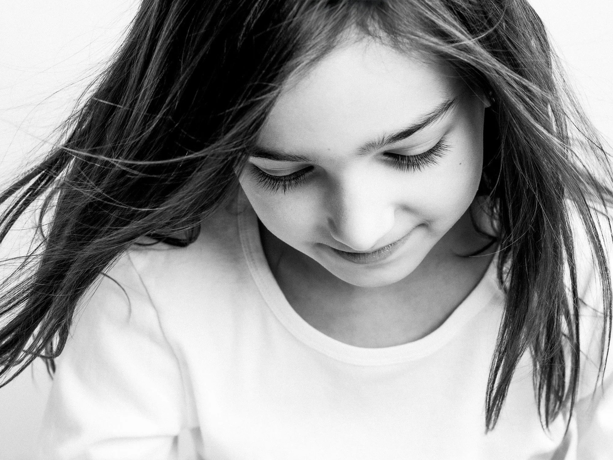 A young girl with long hair looking down, smiling softly, in black and white.