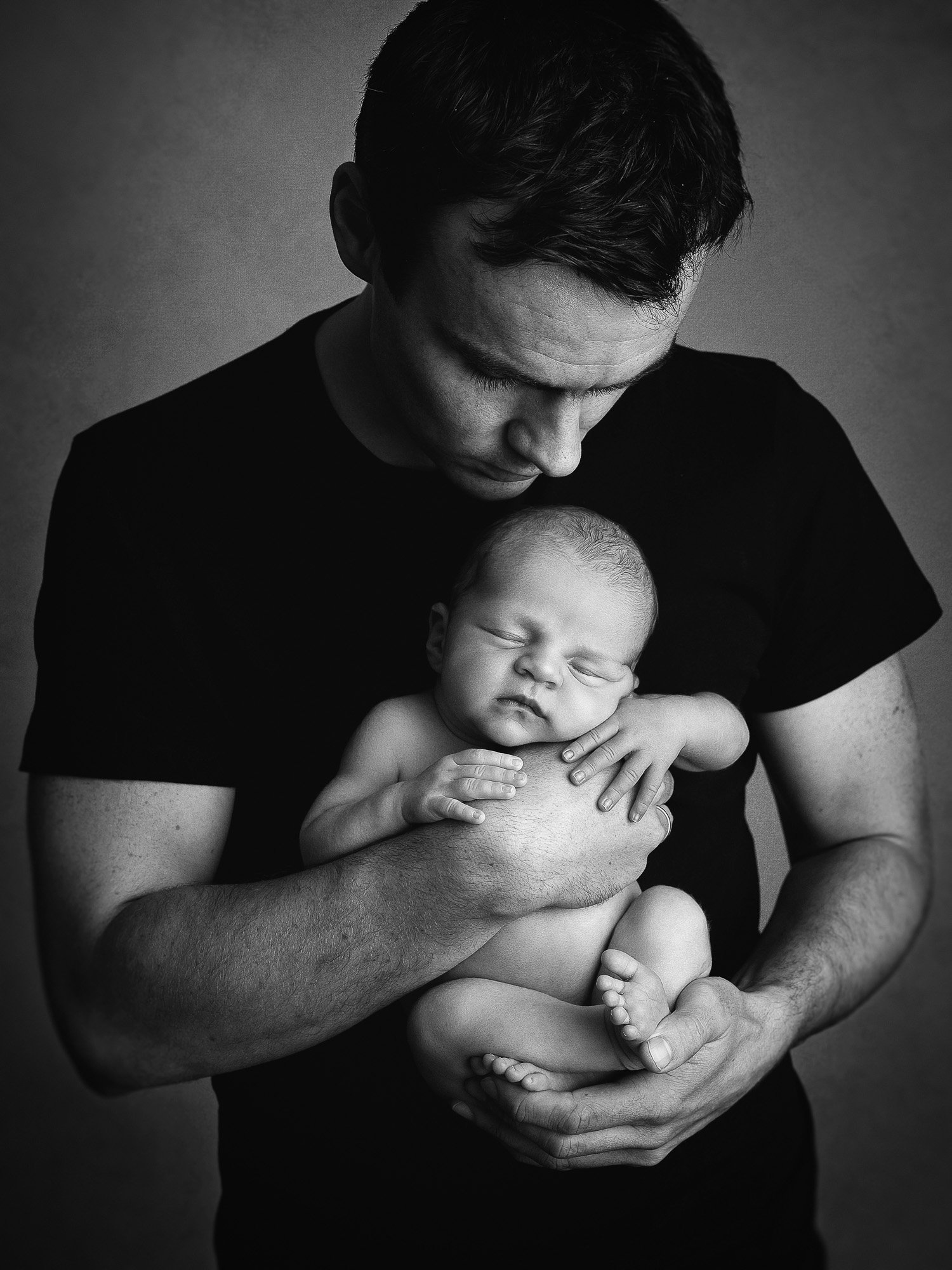 Black and white photo of a man holding a sleeping baby in his arms, gently touching the baby's chest and head.