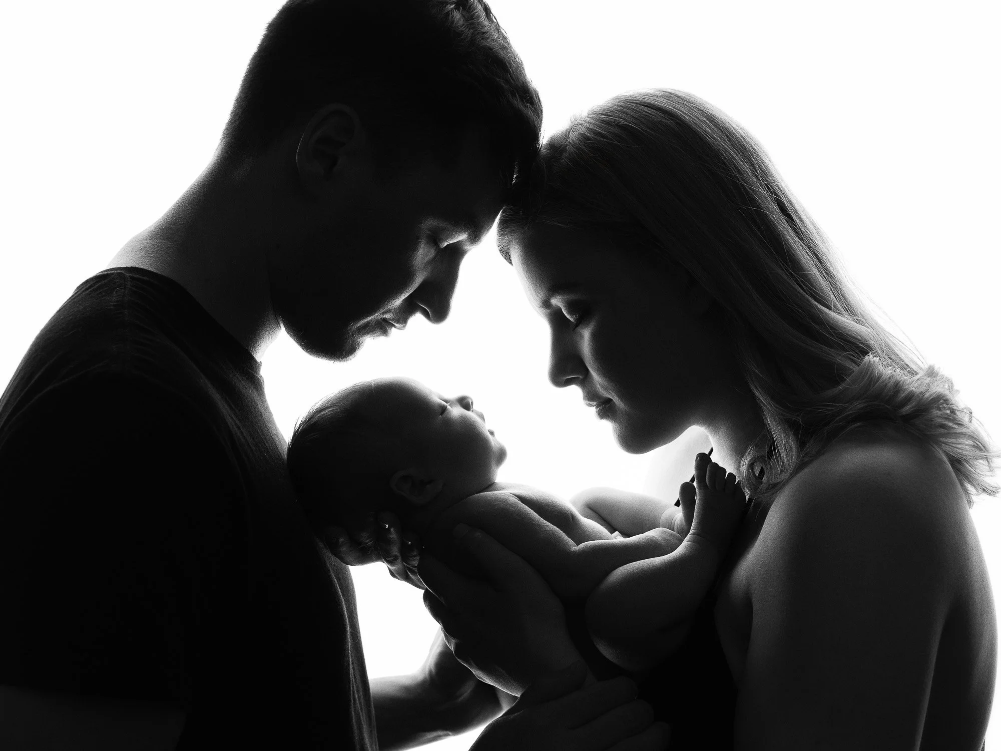 Silhouette of a couple holding their baby, with their foreheads touching, in a tender moment.