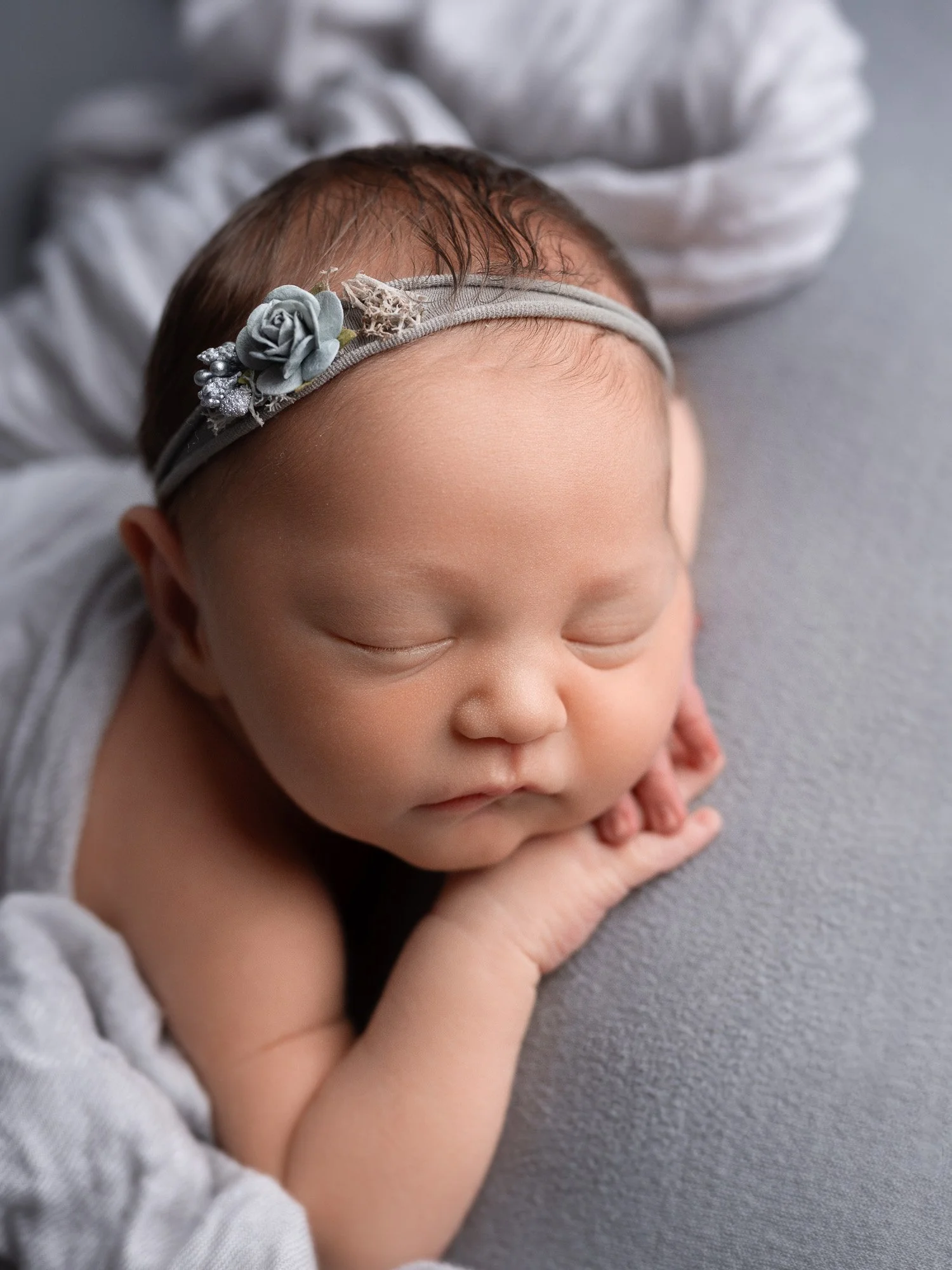 A sleeping baby with a gray flower headband resting on a gray surface.