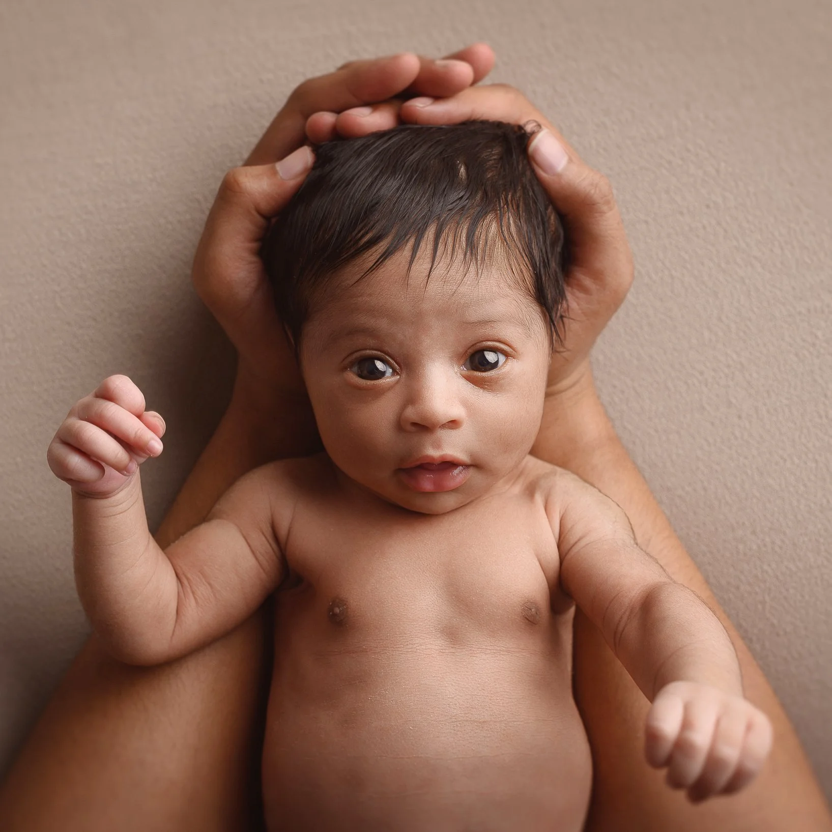 A baby being held by an adult, lying on their back, with the adult's hands supporting the baby's head and shoulders.