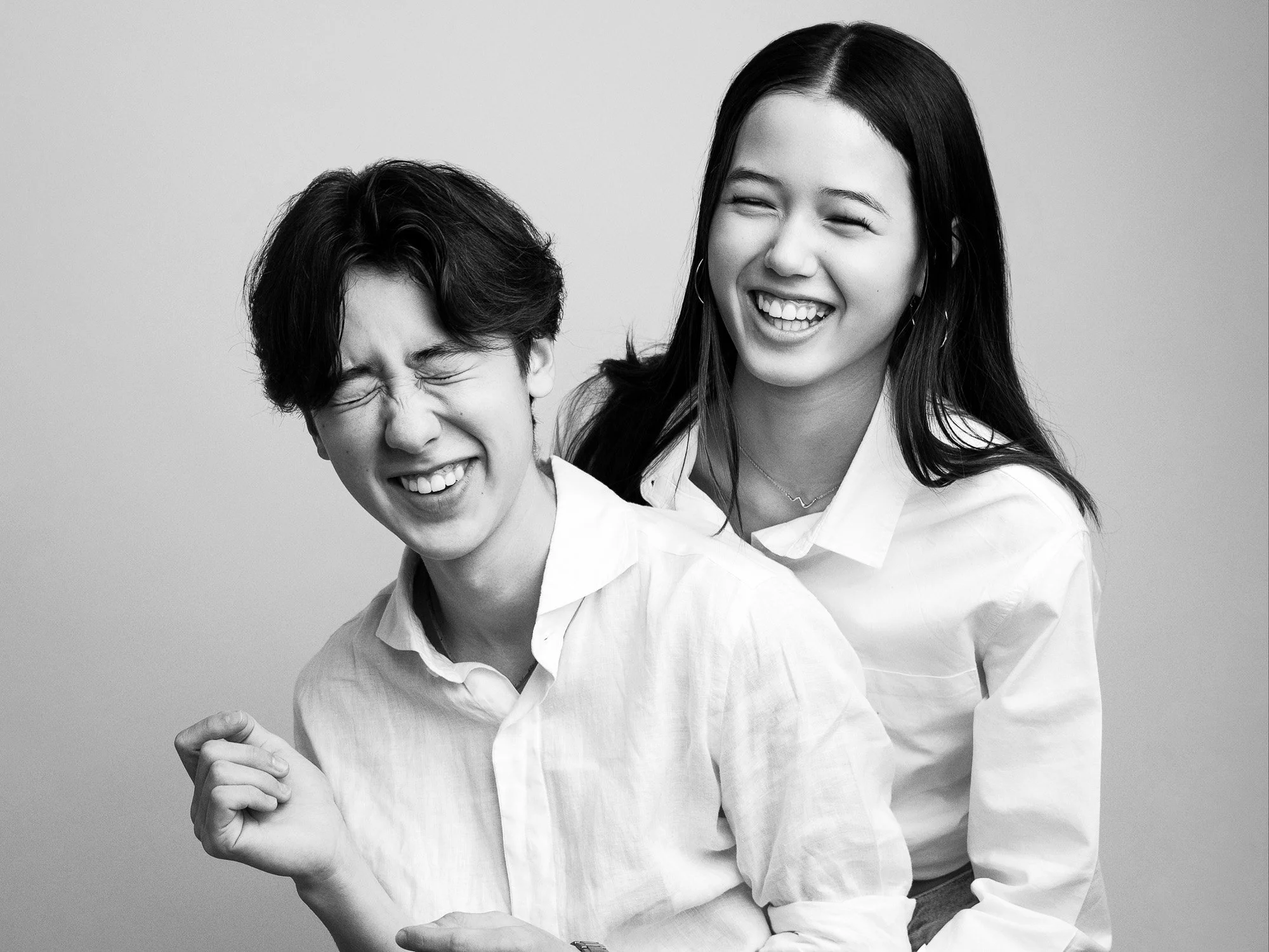 Black and white photo of a young man and woman laughing together, both dressed in white shirts.
