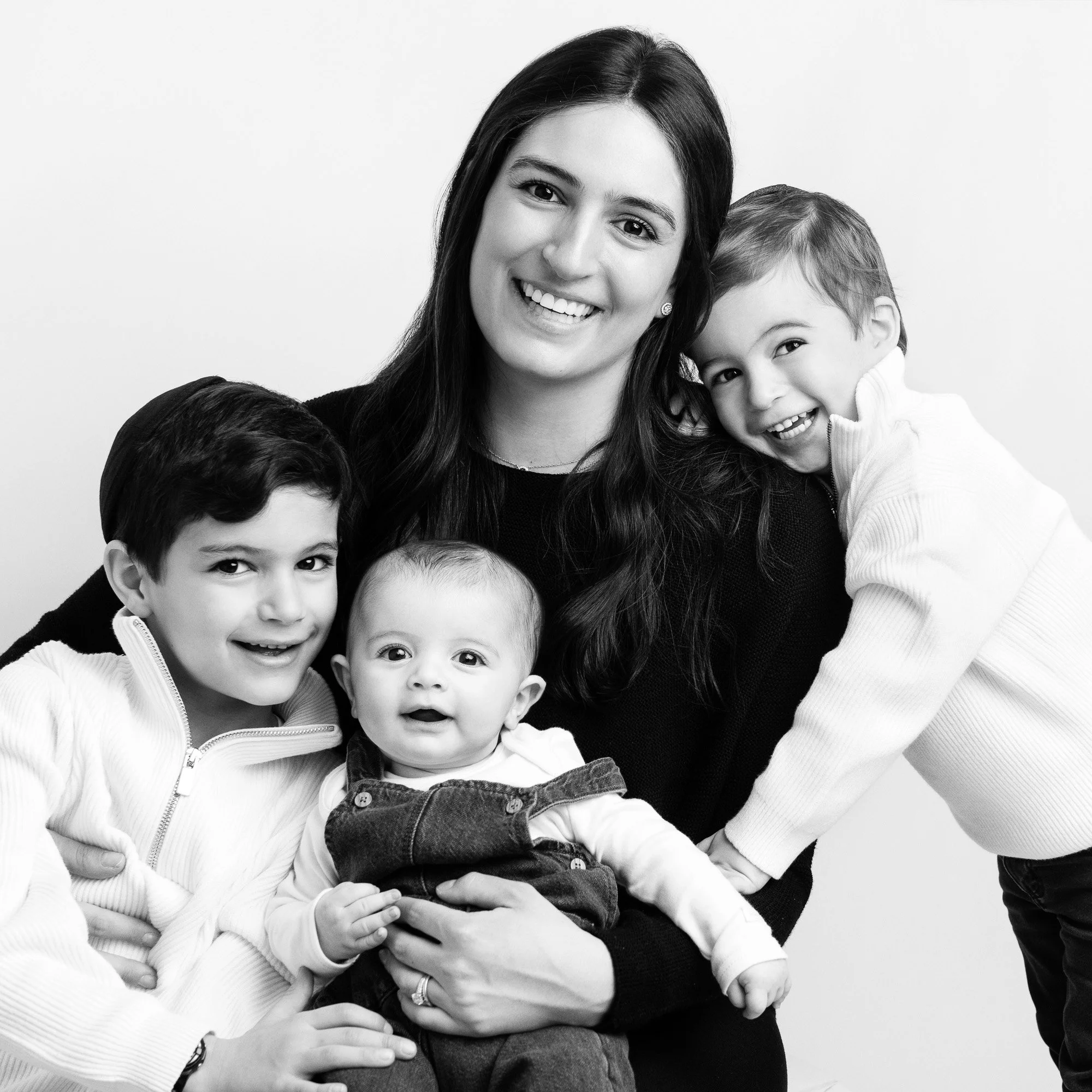 Black and white photo of a woman with three children, smiling and close together, against a plain background.