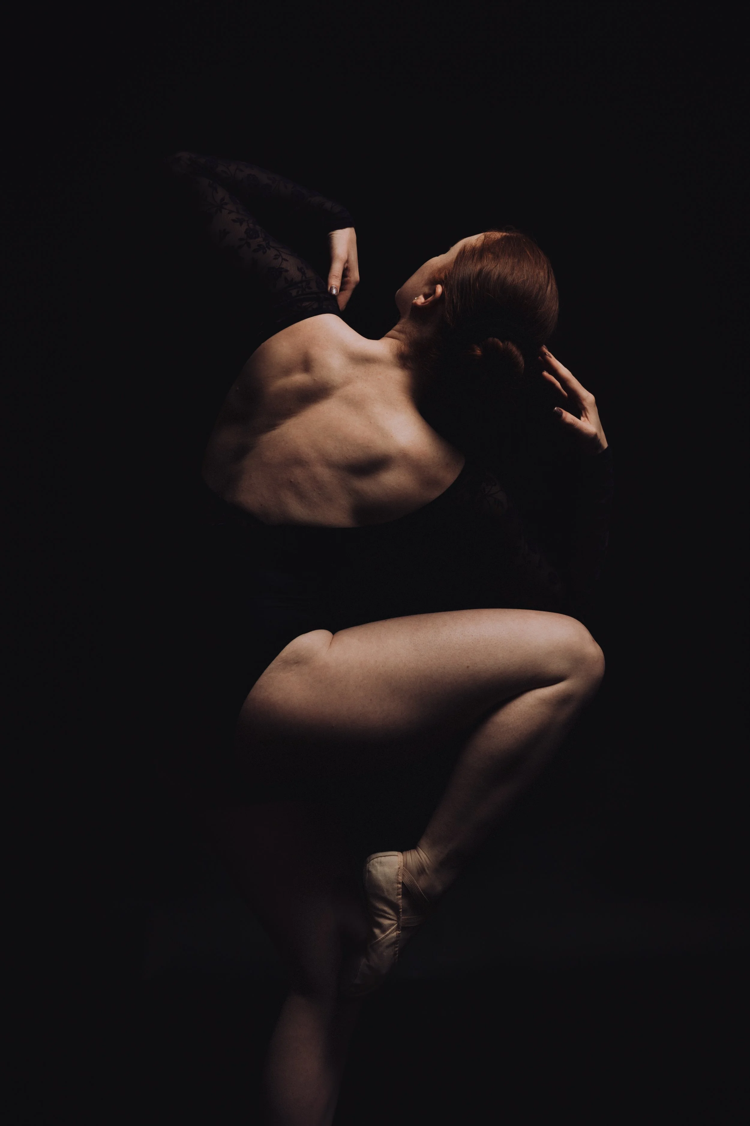 Graceful ballet dancer in a black leotard striking a dramatic pose, highlighting strength and elegance against a dark background