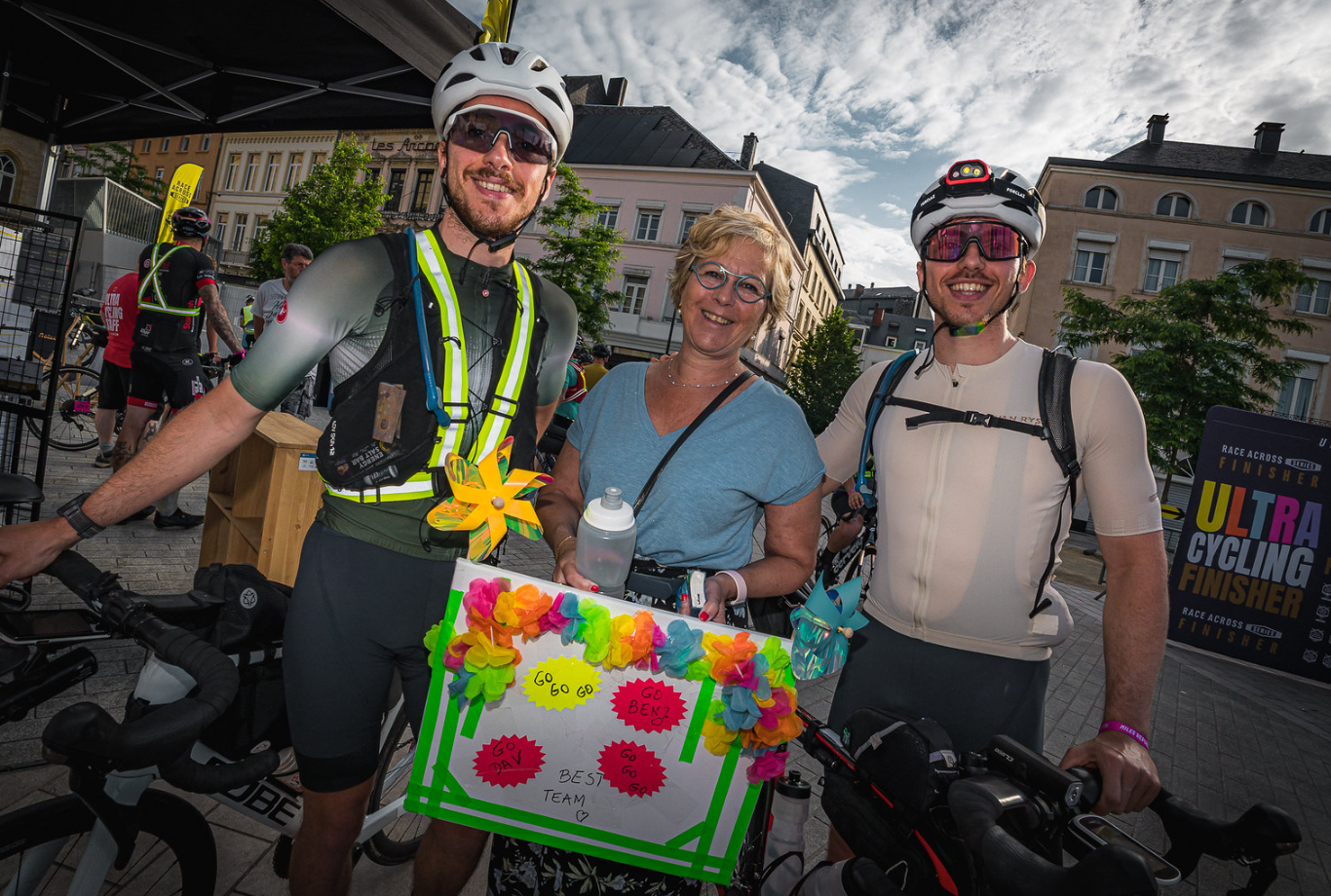 Deux cyclistes, accompagnés d’un proche, échangent un sourire juste avant le départ de la Race Across Series.