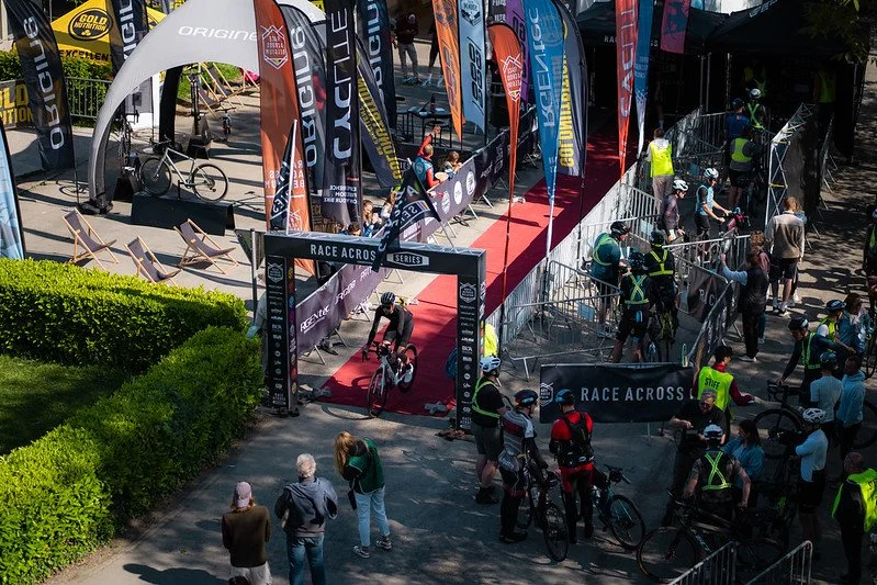 Une scène de course à vélo avec un circuit, des drapeaux, des spectateurs, des coureurs, et des officiels, lors d'un événement organisé.