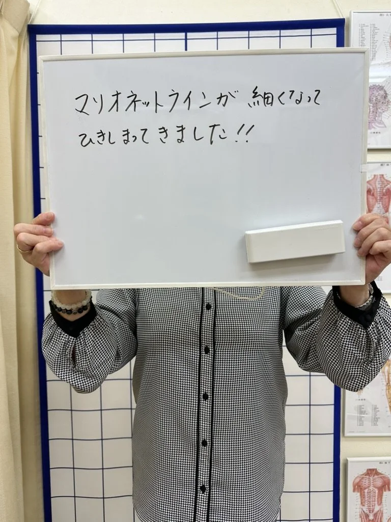60代女性が「マリオネットラインが細くなってひきしまってきました」と手書きしたボードを持っている写真