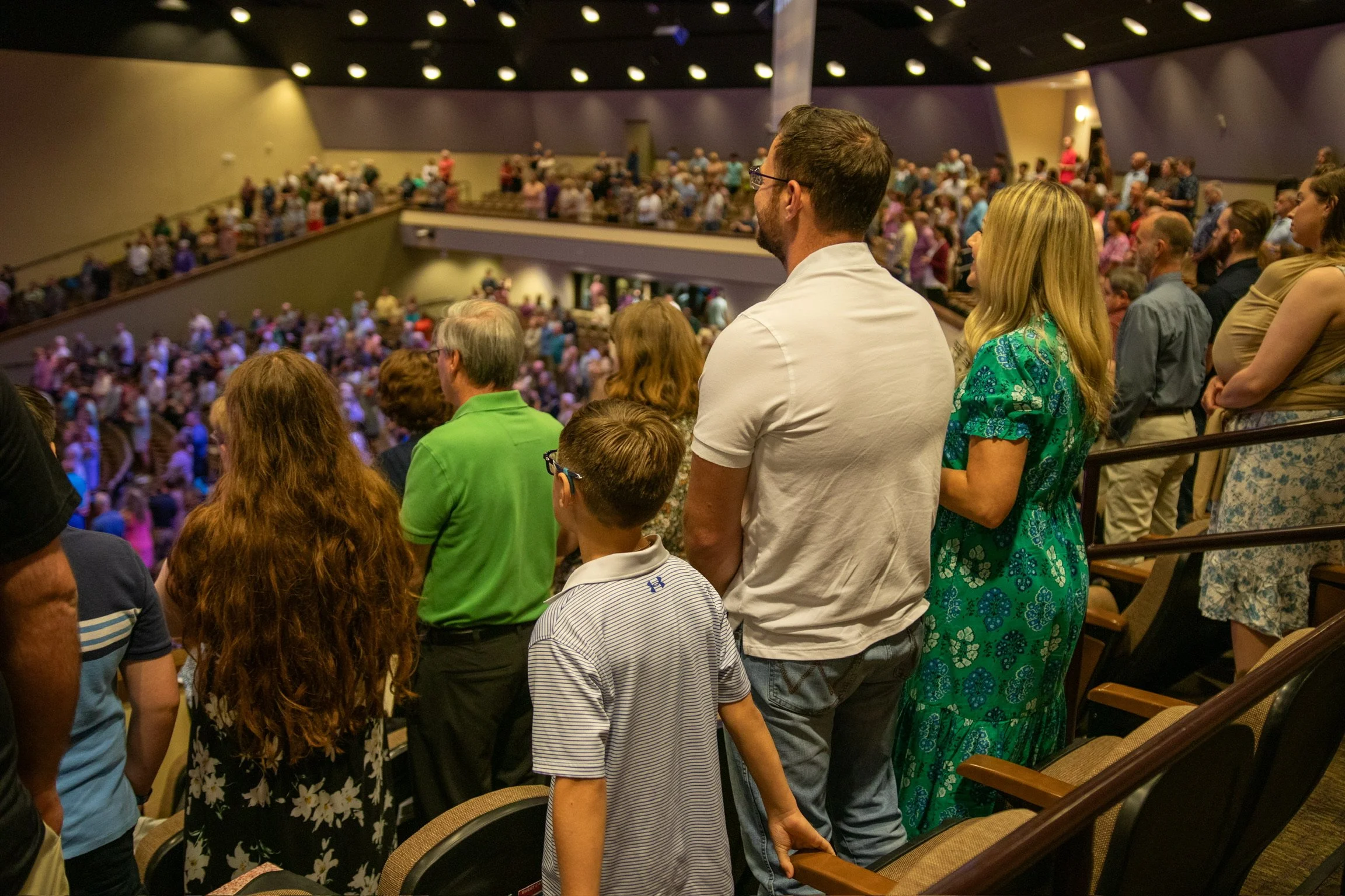 People standing in auditorium seats watching a presentation or event.