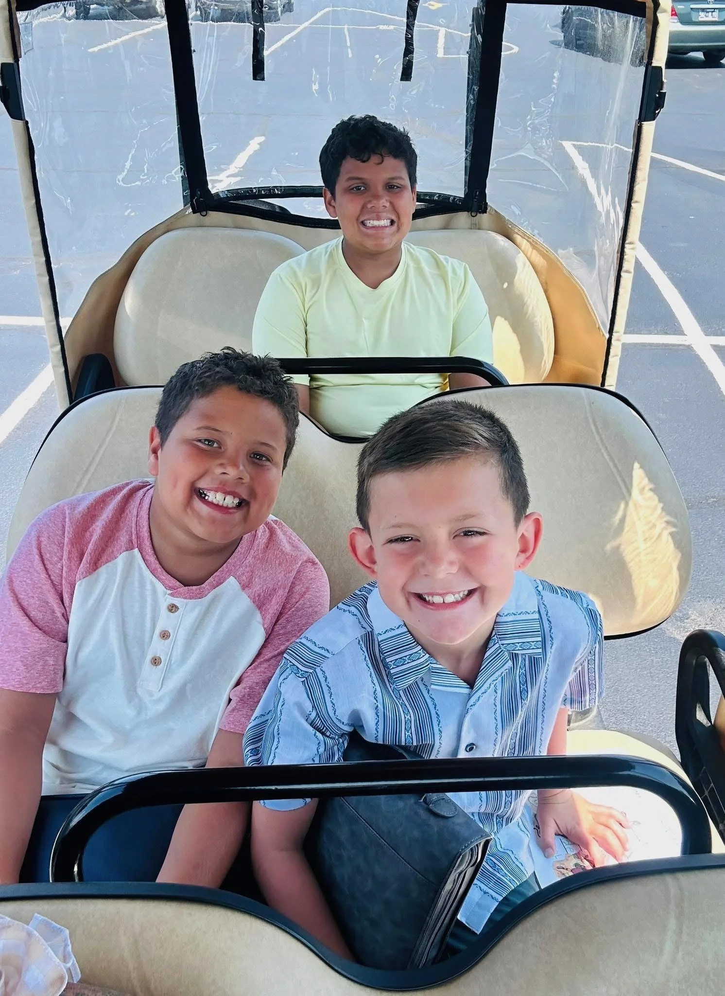Three boys sitting in a golf cart, smiling happily at the camera.