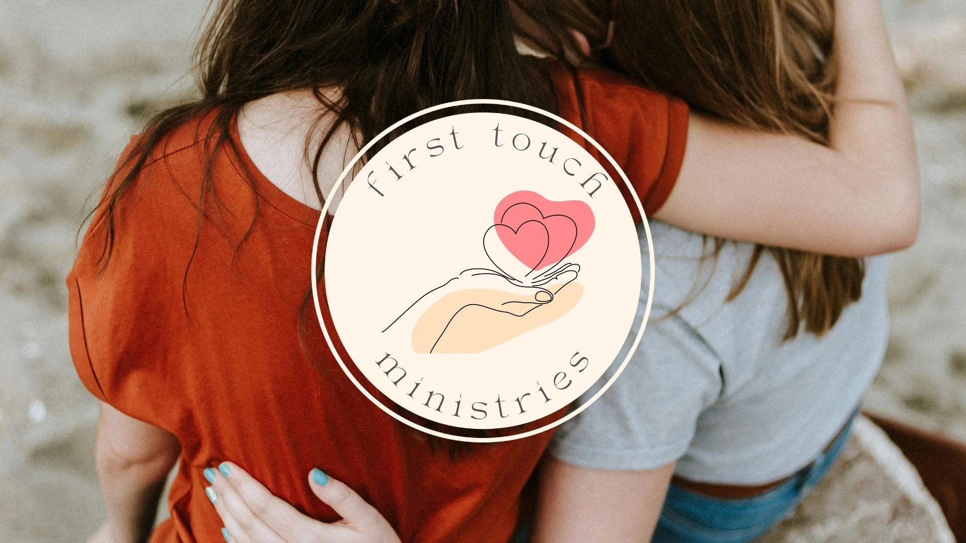 Two women hugging on a beach, with a circular logo overlay that says 'first touch ministries' and features a hand holding hearts.