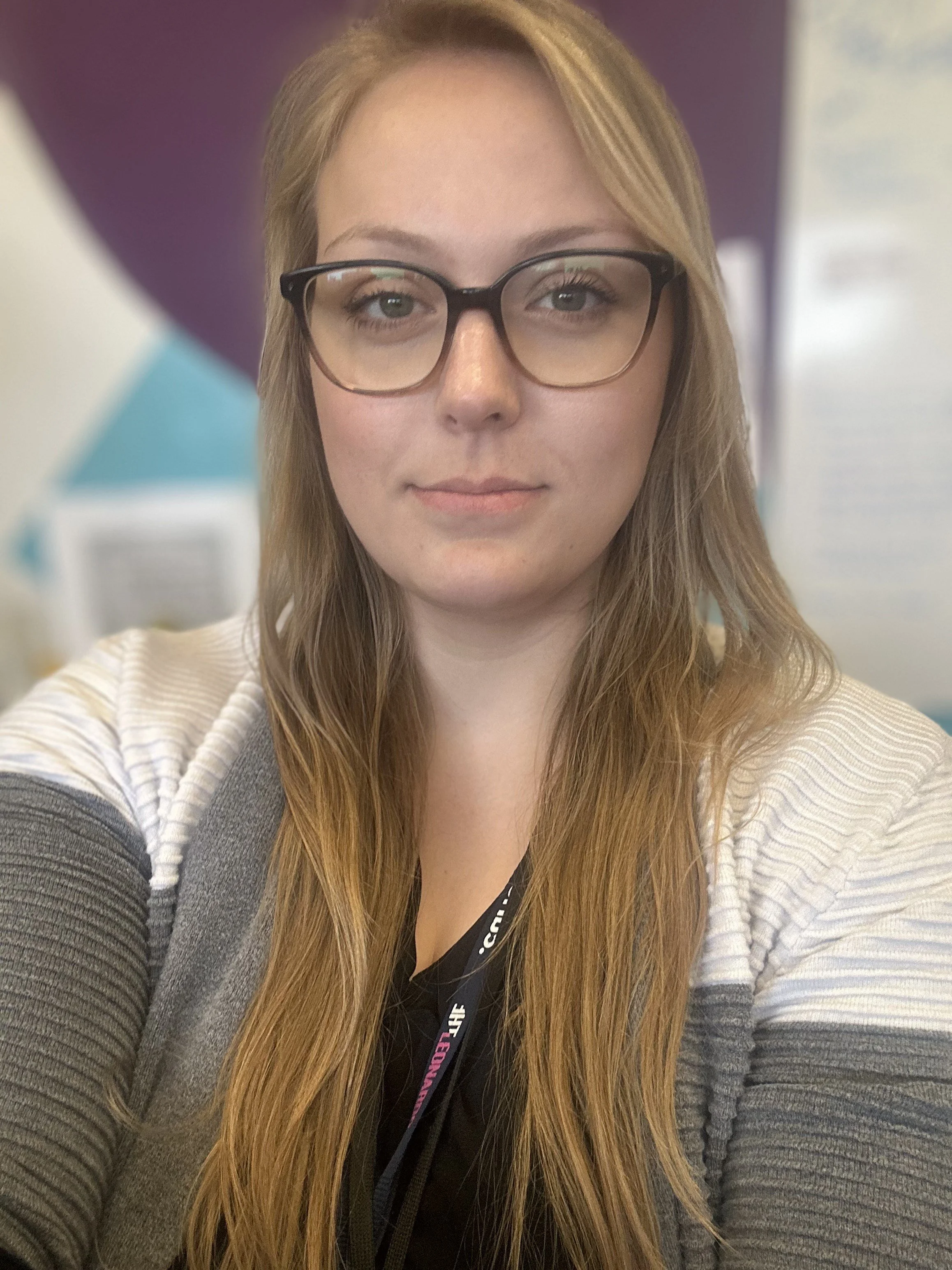 Corban Barbuto, owner of Barbuto Bookkeeping Inc. She is an accountant of over 5 years. A young woman with long red hair, wearing glasses and a black shirt, taking a selfie in an indoor setting with purple and light-colored walls.
