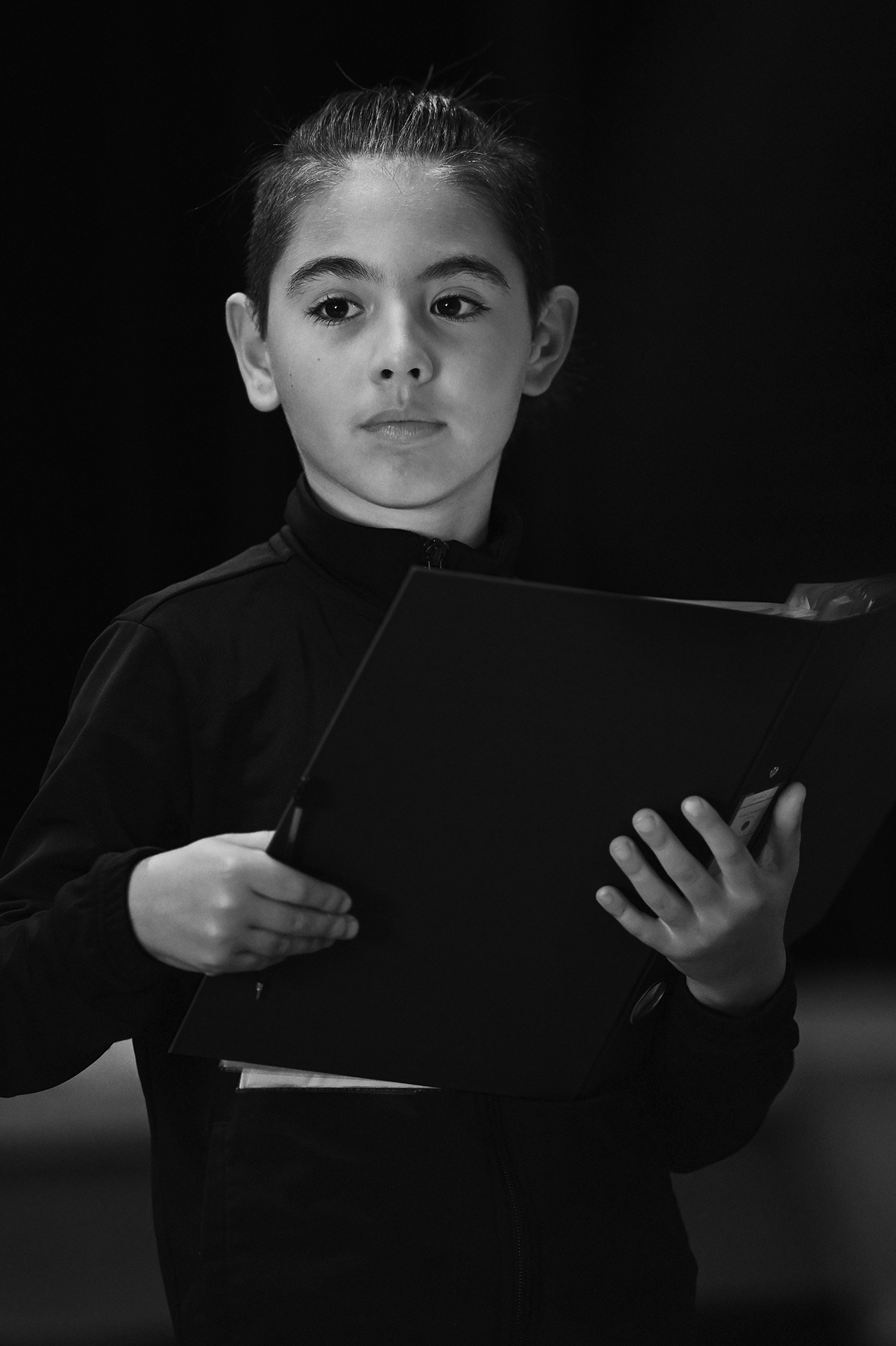 A young person holding a folder, looking thoughtfully into the distance, in a black and white photo.