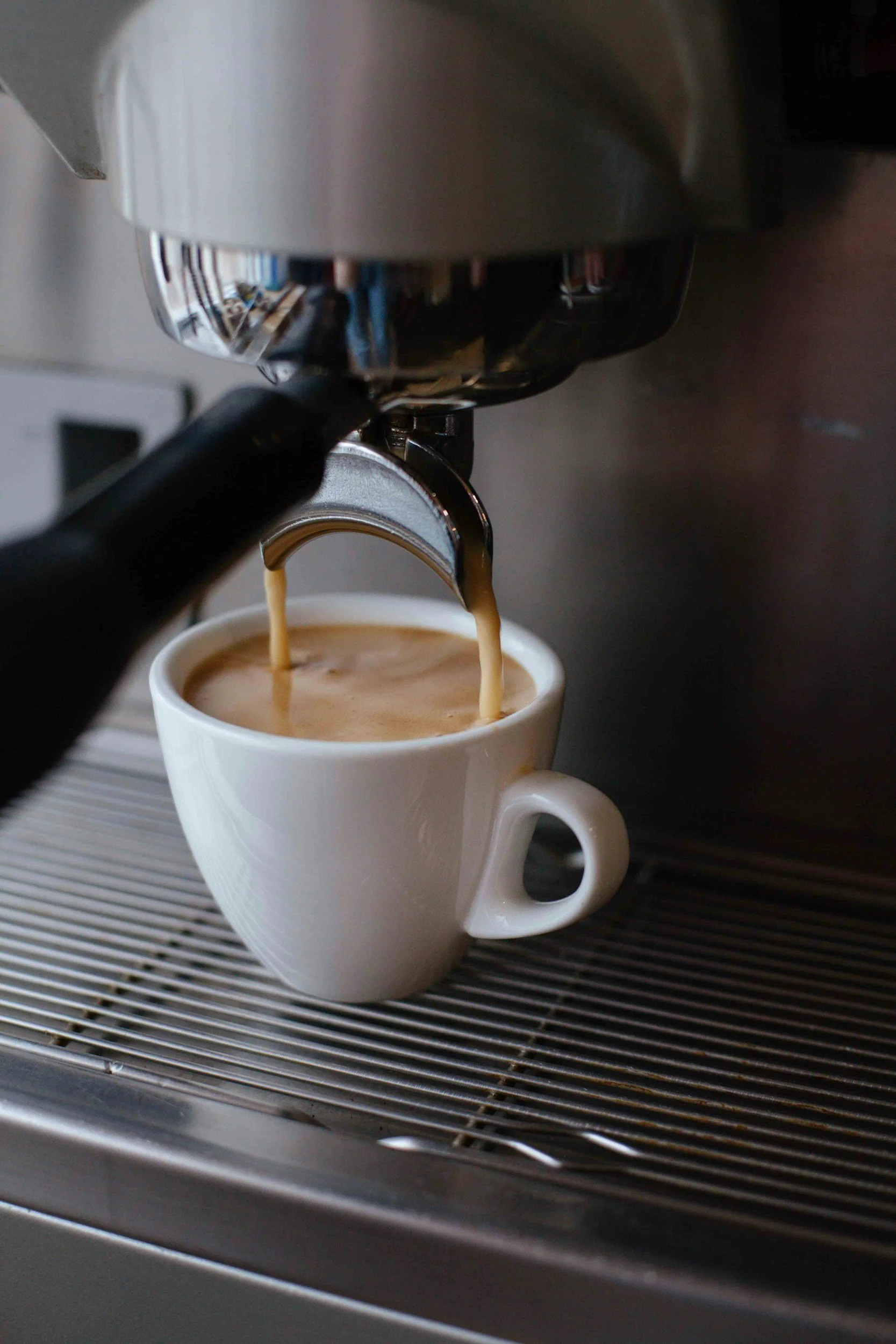A close-up of an espresso machine pouring coffee into a white cup on a metal drip tray.