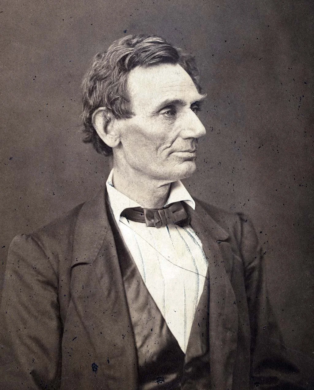 Black and white vintage portrait of a man with wavy hair, wearing a suit with a bow tie, in a serious pose.