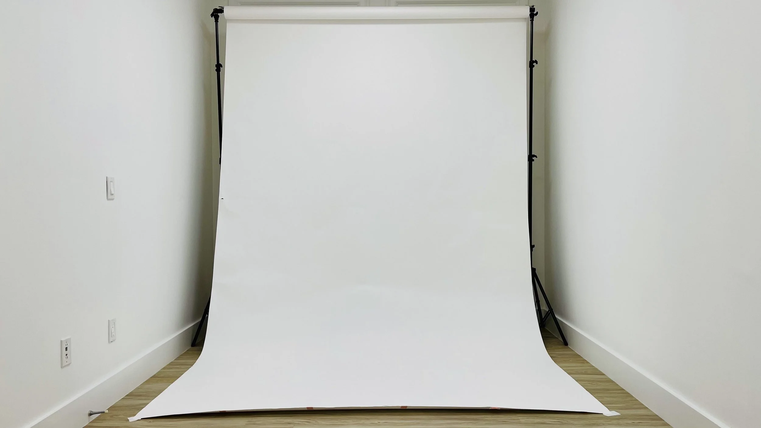 Photo of a white paper backdrop on a stand in a room with white walls and wood flooring.