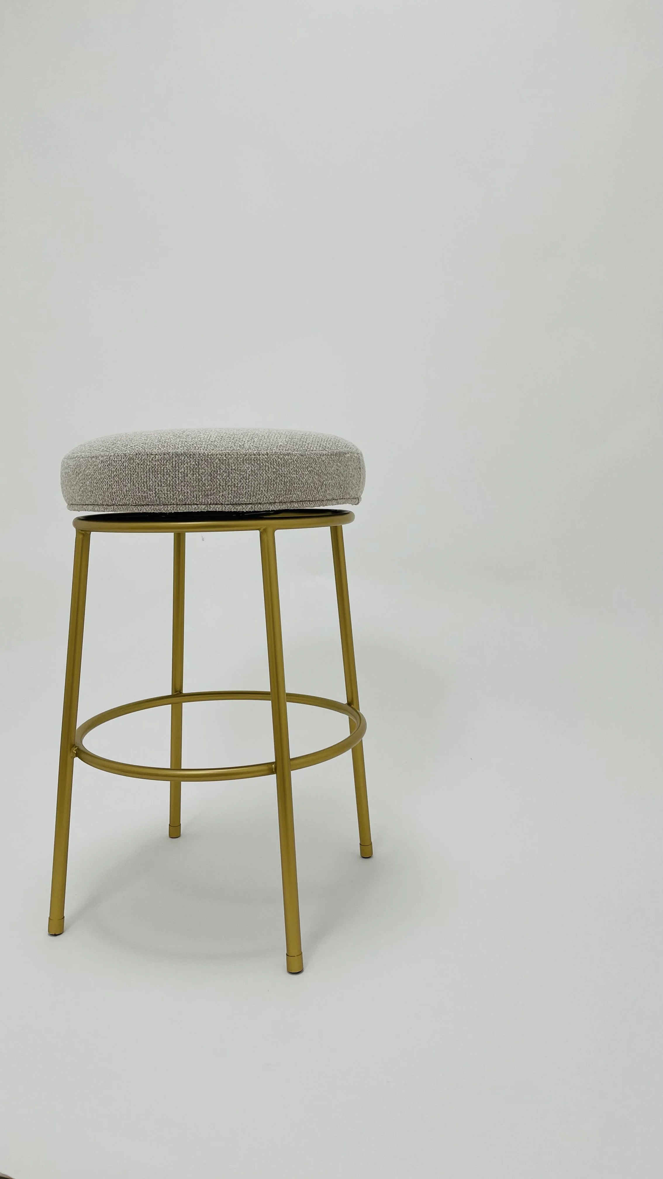 A modern stool with a beige cushioned seat and gold metal frame against a plain white background.