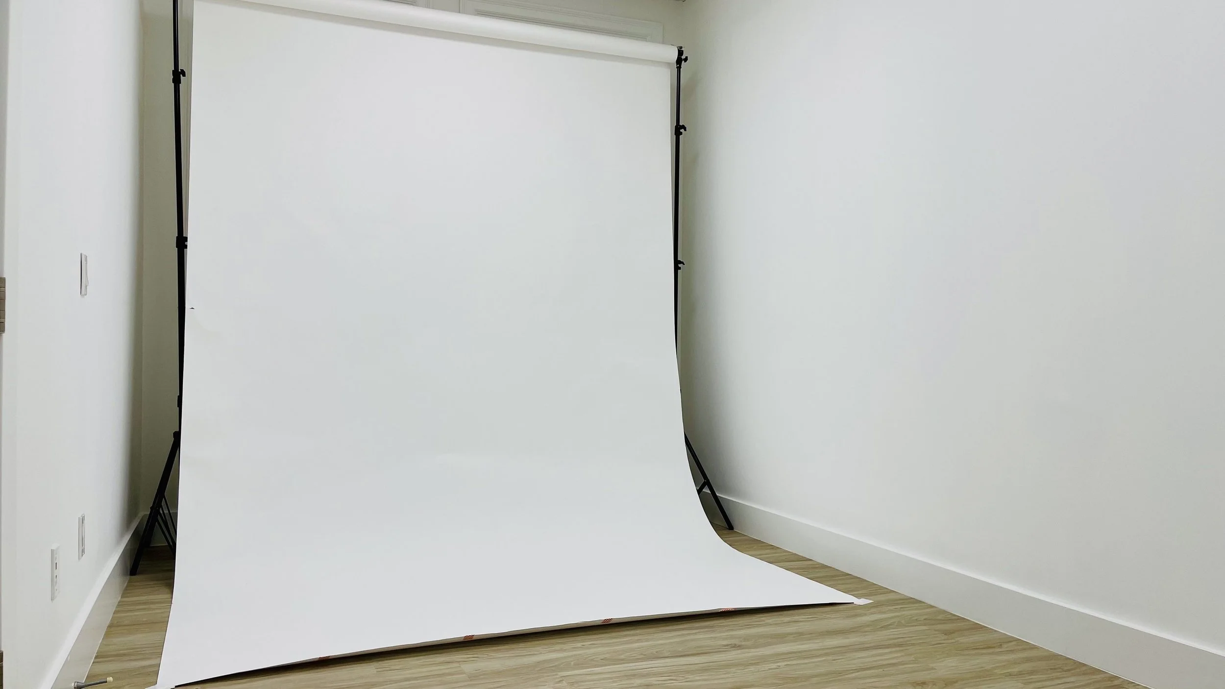 Photo of a white backdrop on a stand in a room with wood flooring and white walls.