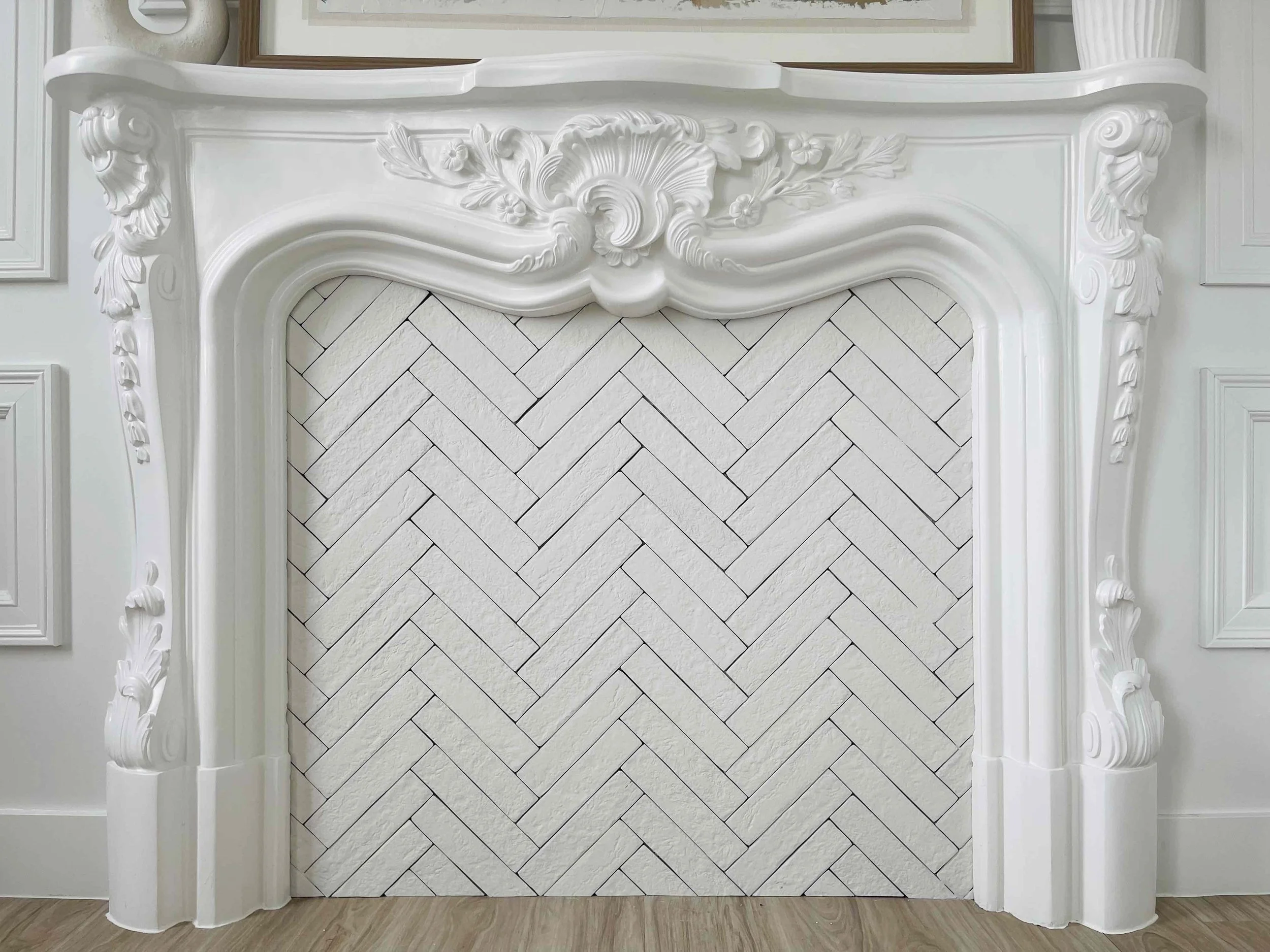 White ornate fireplace with intricate carvings and a chevron-patterned white tile interior.