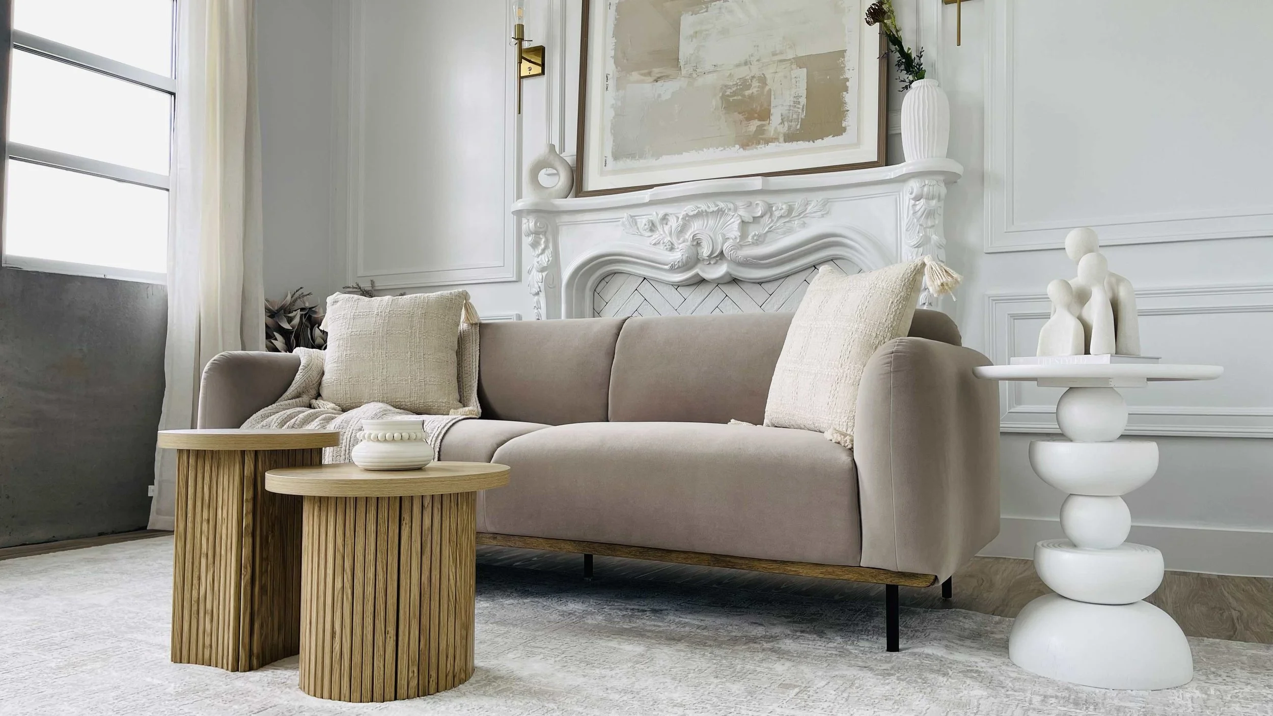 Living room with beige sofa, wooden coffee tables, white decorative vase, and abstract artwork on the wall.