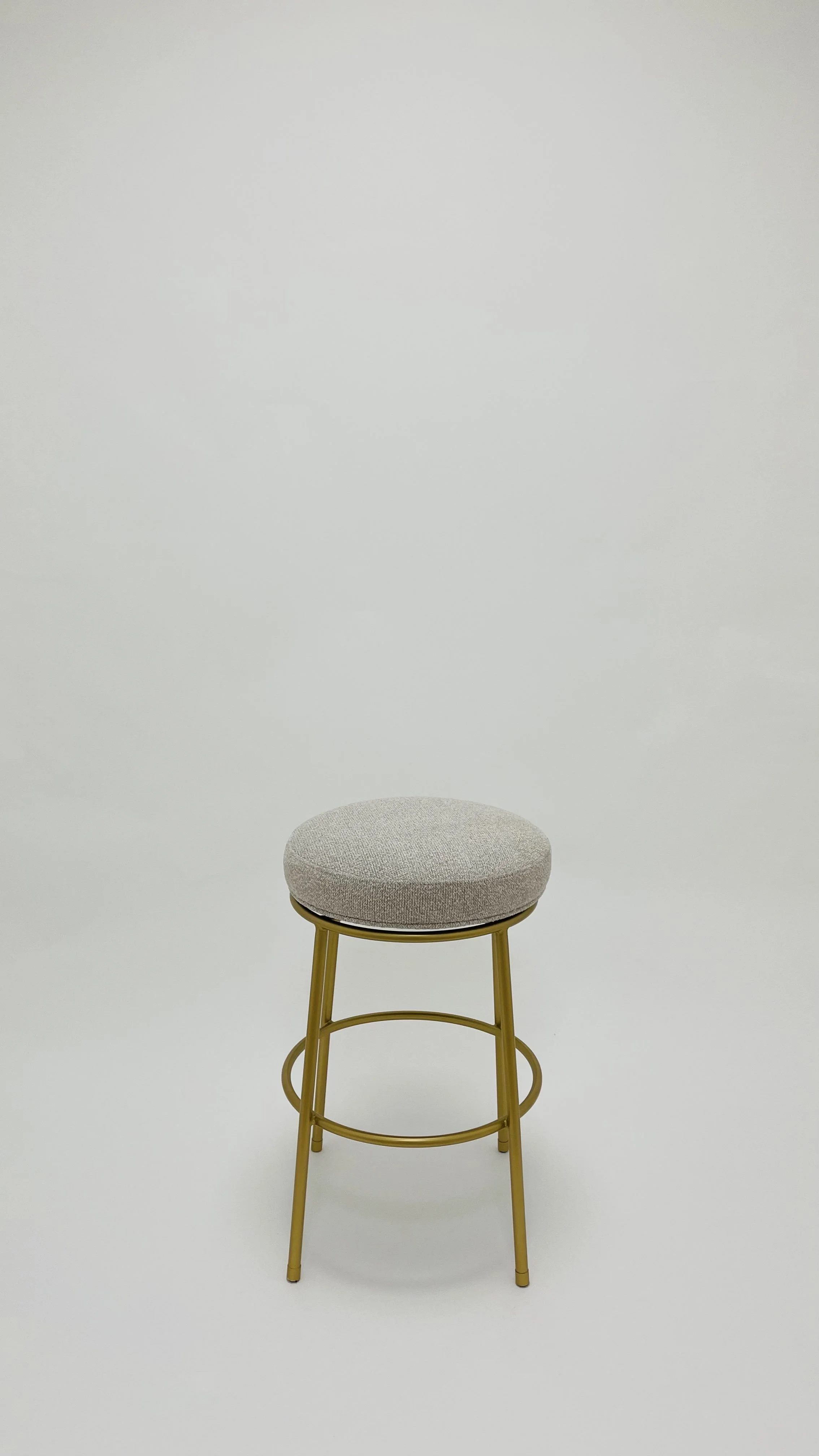 A beige upholstered stool with gold metal legs against a plain white background.