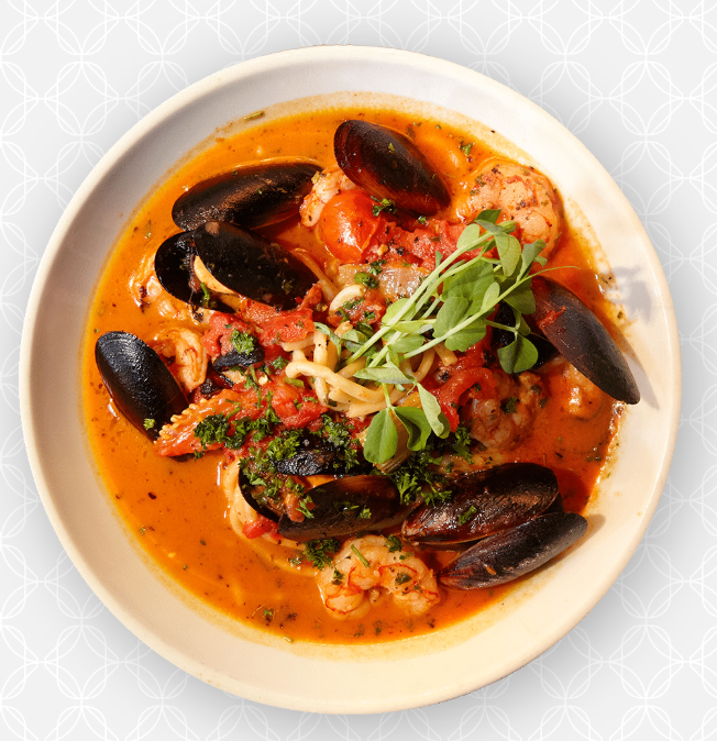 Seafood soup with mussels, shrimp, and garnished with herbs and greens in a white bowl.