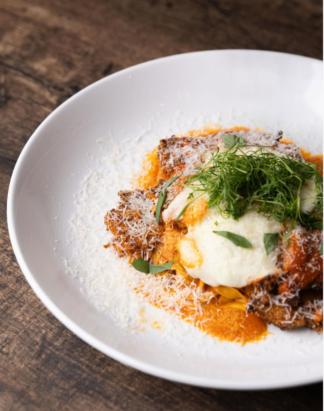 Pasta dish with tomato sauce, shredded cheese, fresh herbs, and a dollop of cream, served in a white bowl on a wooden table.