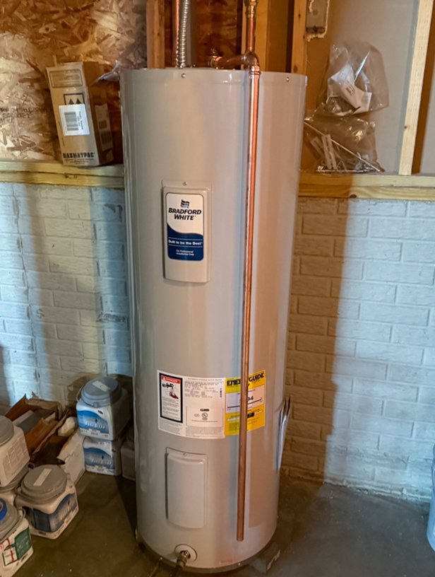 A Bradford White water heater installed in a basement, surrounded by various containers and supplies.